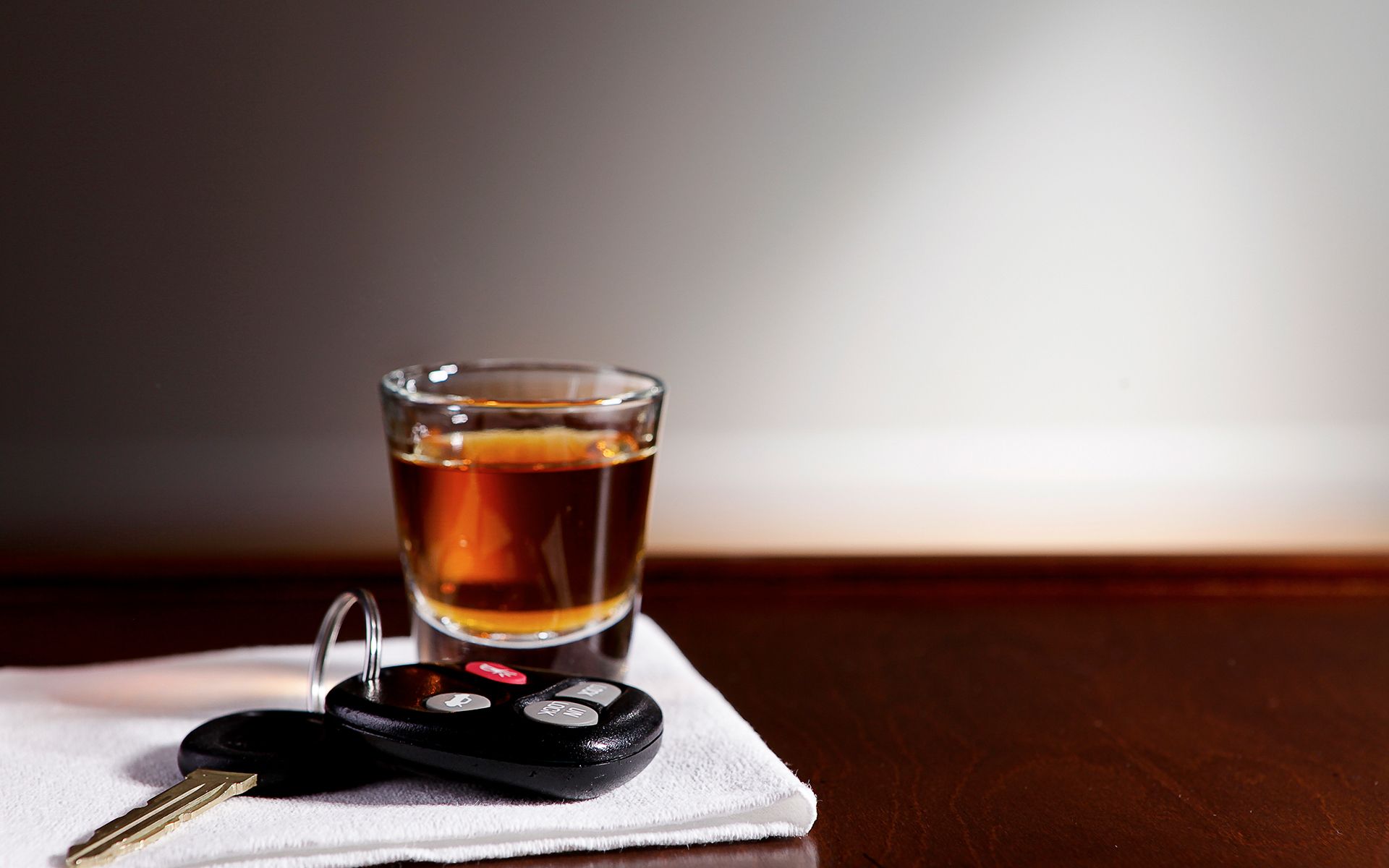 A car key and a shot glass of alcohol on a table.
