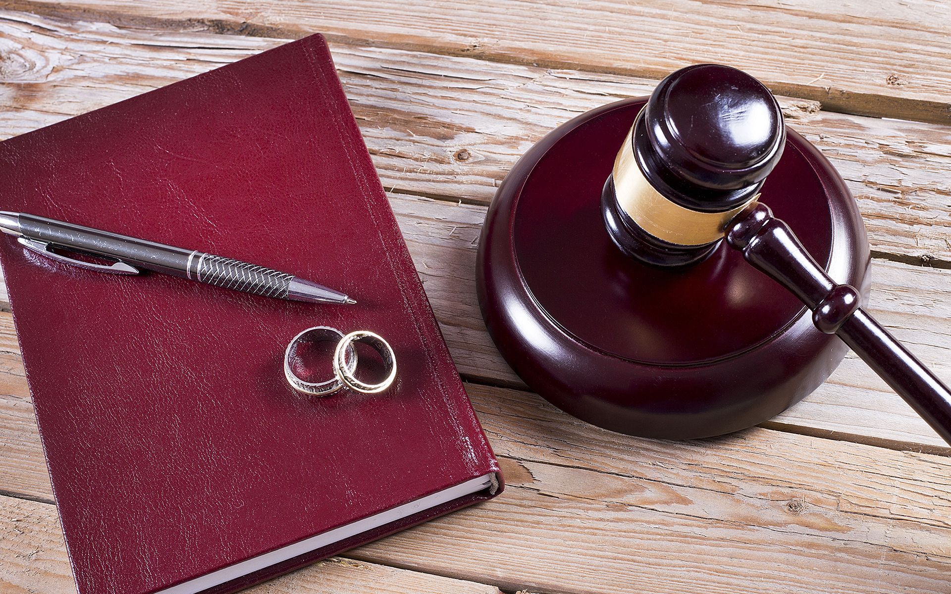 A pair of wedding rings , a pen , and a judge 's gavel on a wooden table.
