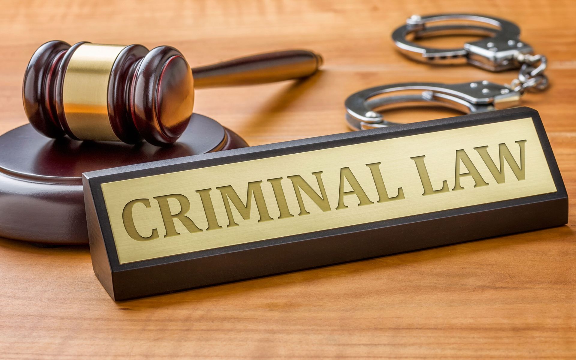 A wooden sign that says criminal law next to a judge 's gavel and handcuffs.
