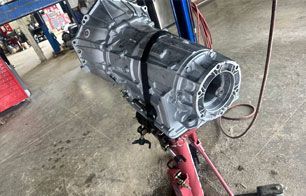 Silver car transmission on a red jack in a garage.