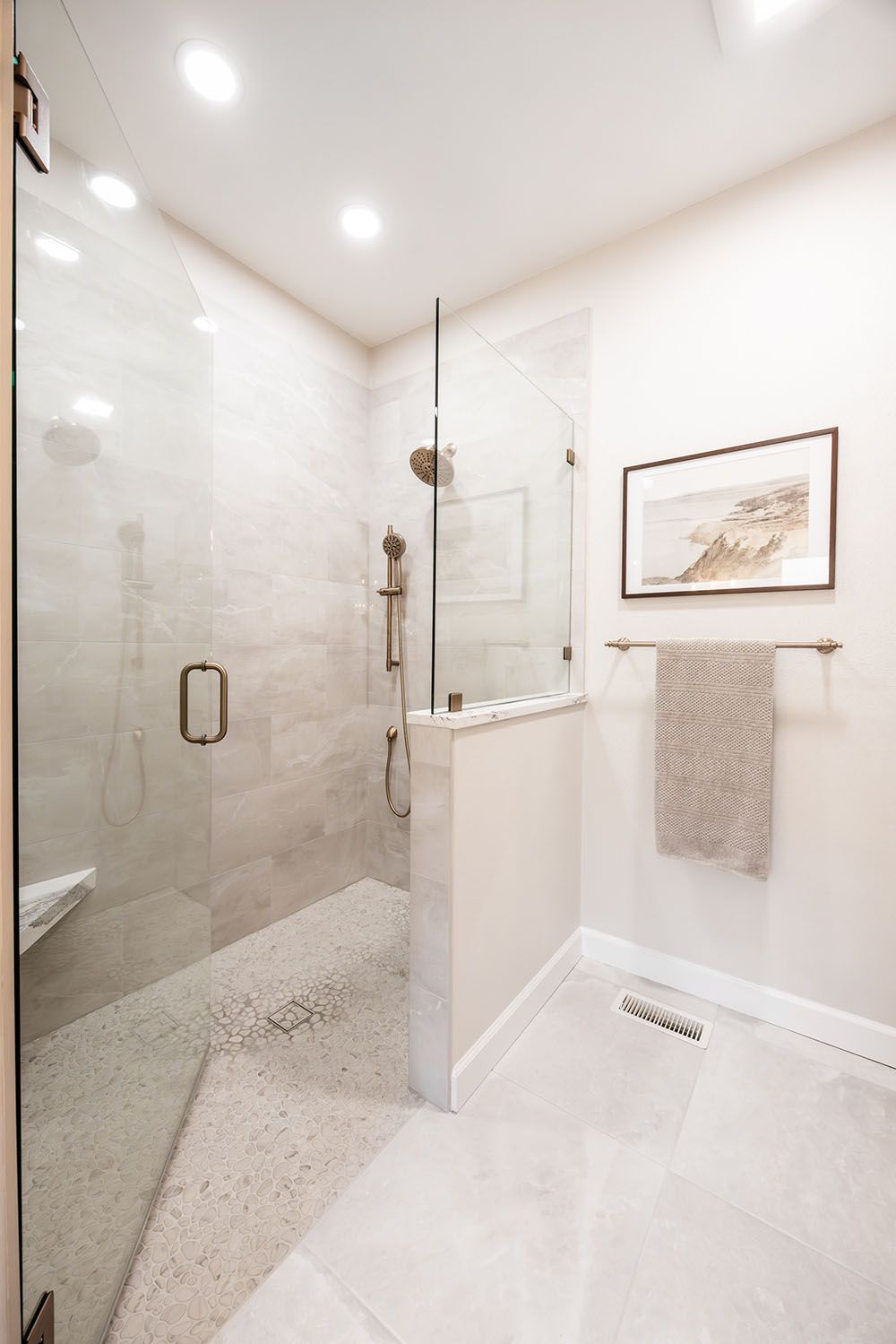 A modern bathroom with a glass-enclosed shower, stone pebble floor, white walls, and a towel on a wall-mounted rack.