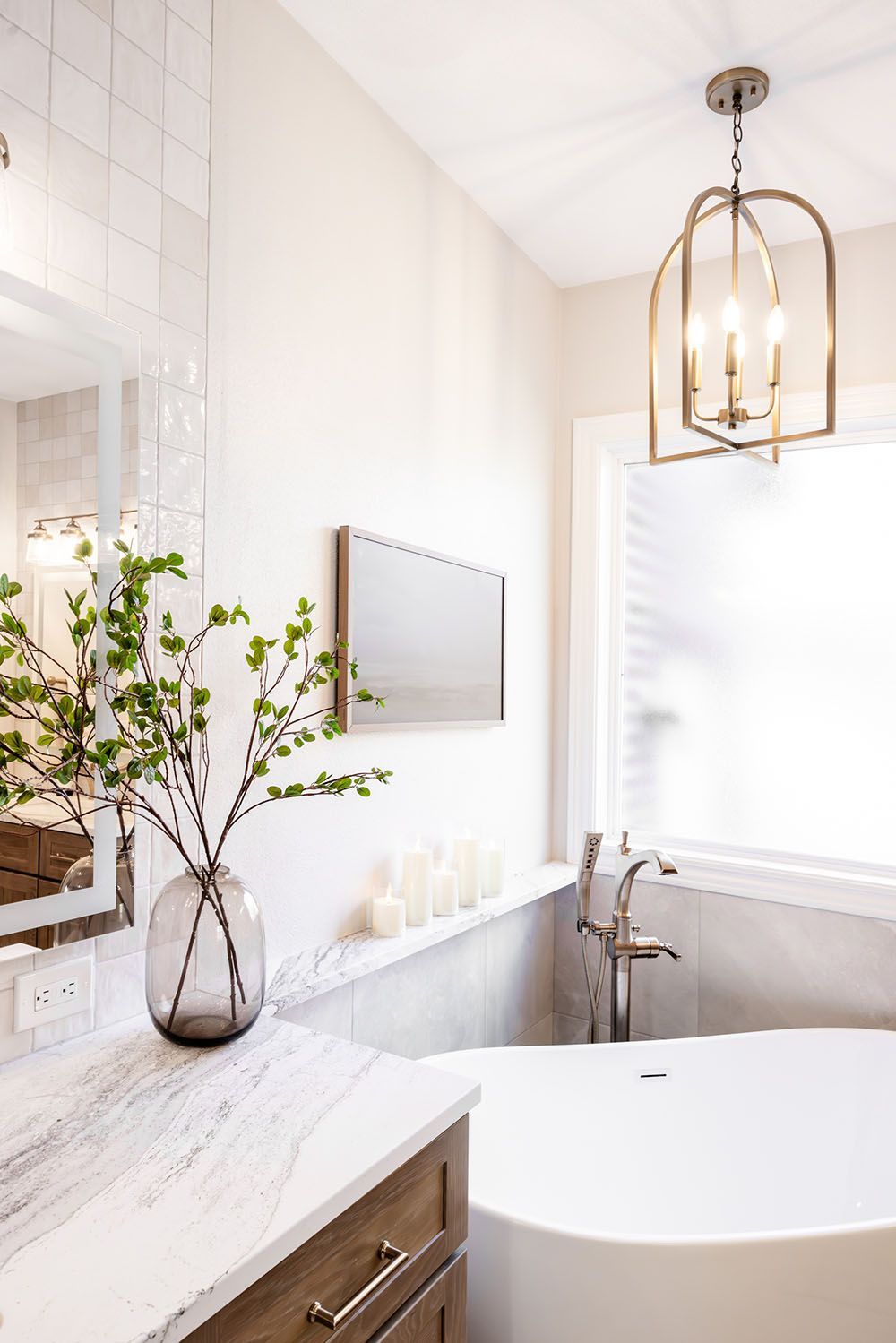 Modern bathroom with marble vanity, a glass vase with greenery, white soaking tub, and a hanging lantern light fixture.
