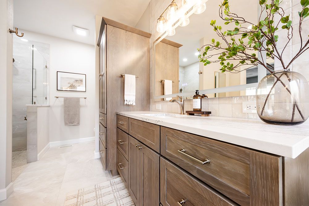 Modern bathroom featuring a wood vanity with a white countertop, large mirror, and a glass-enclosed shower in the rear.