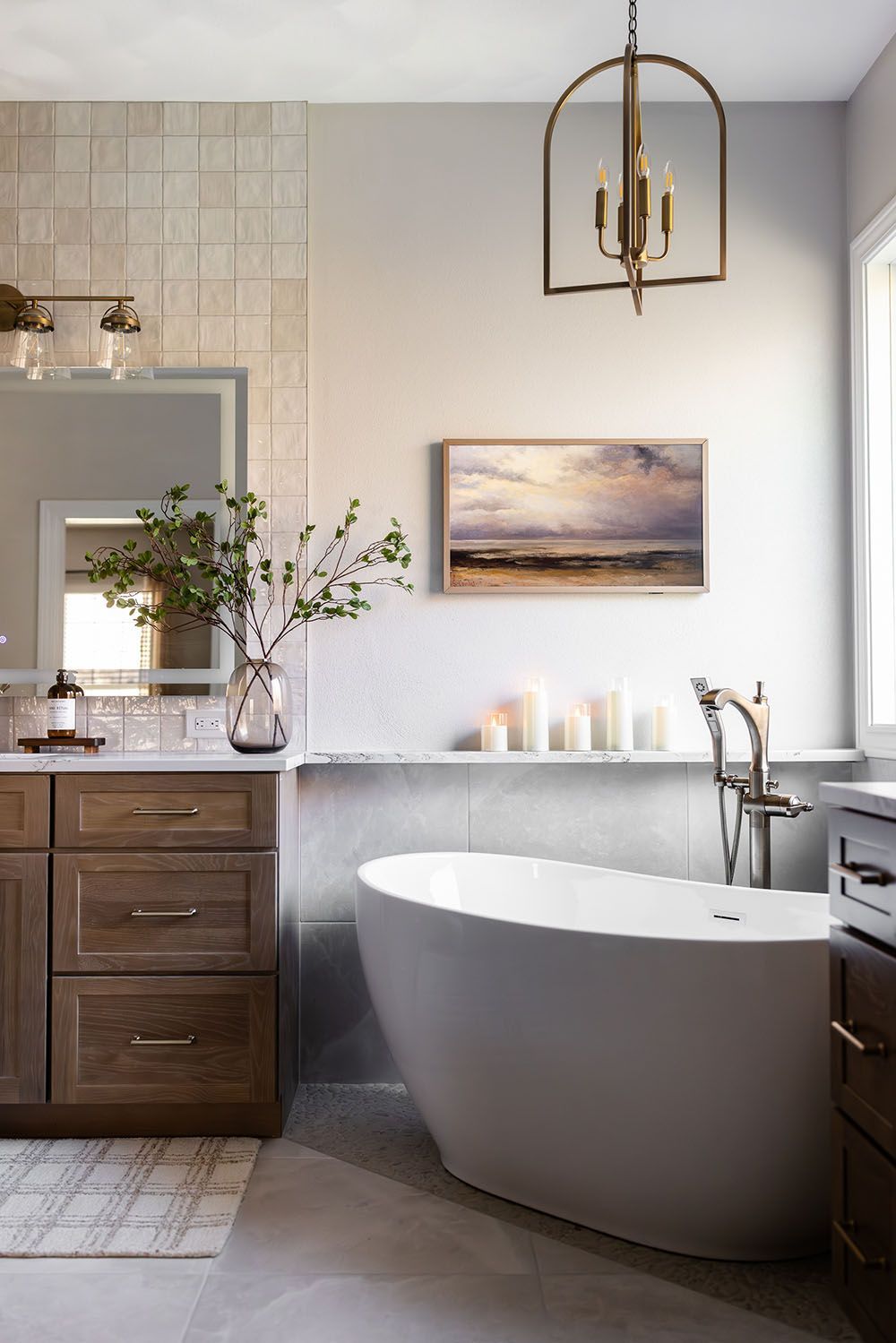 Modern bathroom featuring a wood vanity, white freestanding bathtub, lantern pendant light, and coastal-style wall art.