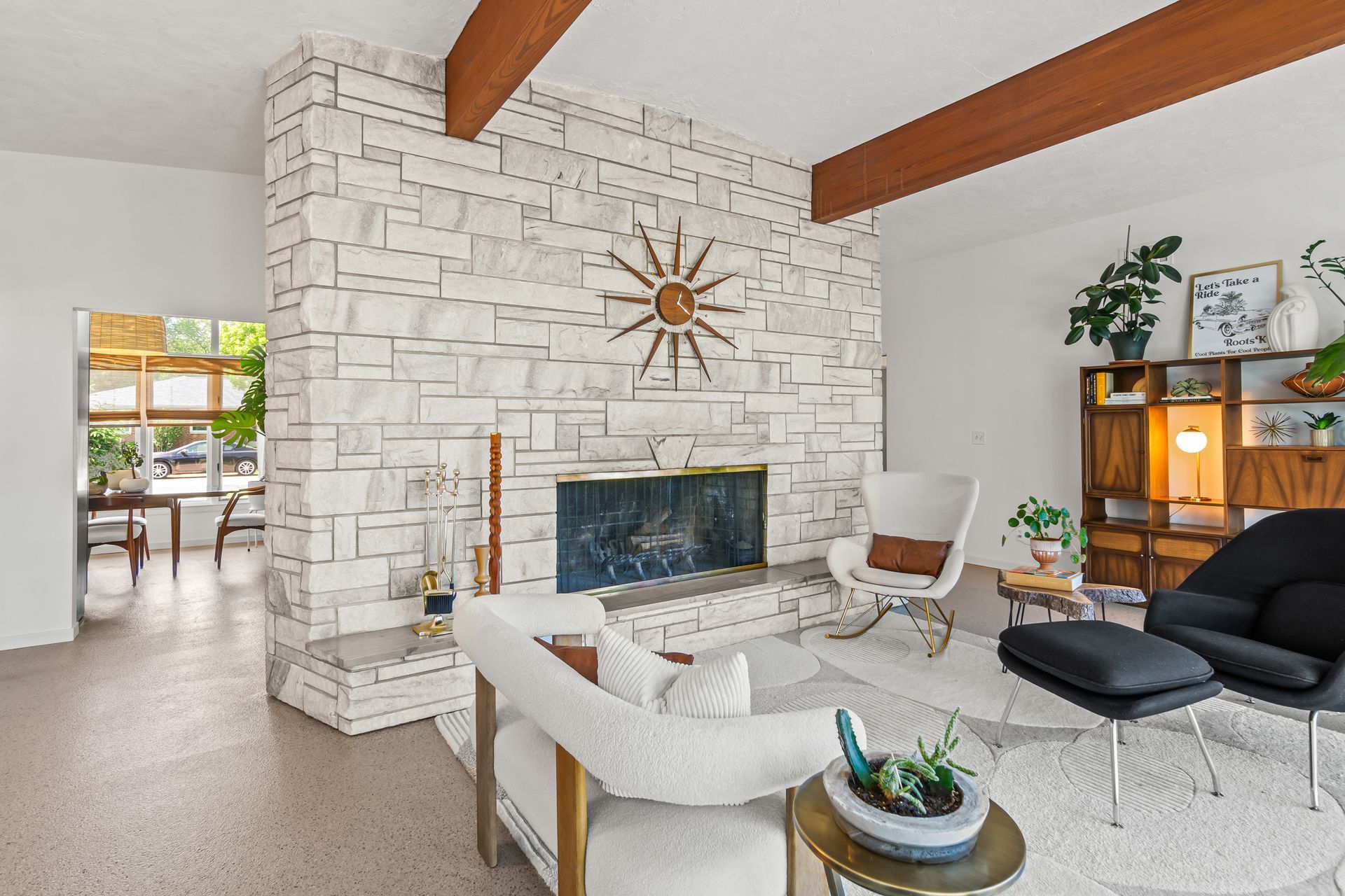 Bright living room with white stone fireplace, wood beams, and black-and-white seating arrangement