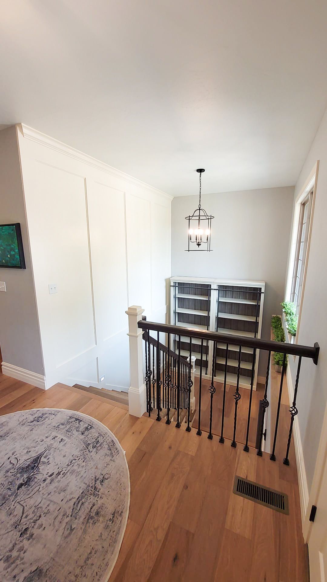 Bright hallway with wood floors, black railing, white walls, and a dining table near a window.