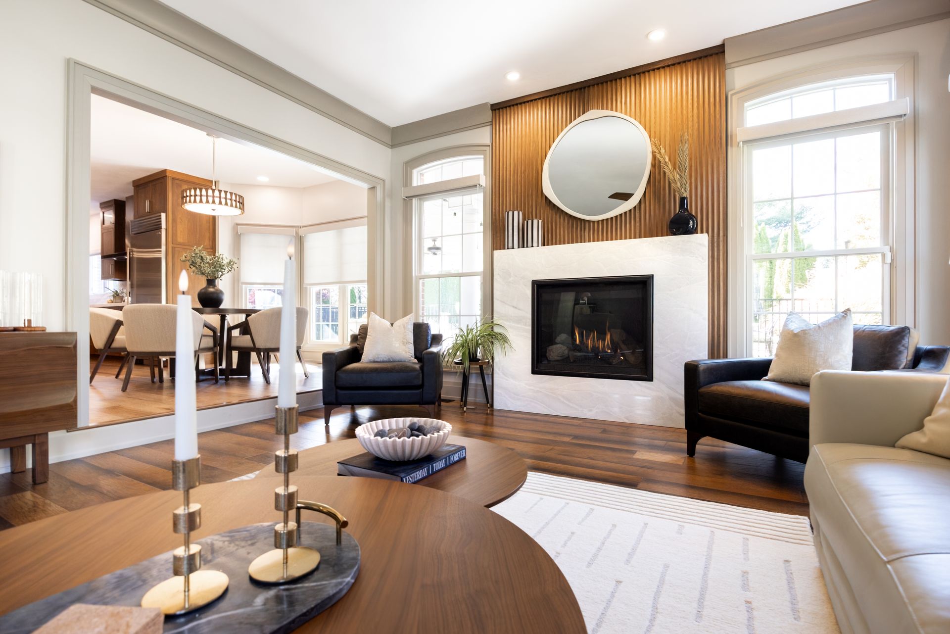 Bright living room with a fireplace, black chairs, large windows, and warm wood floors