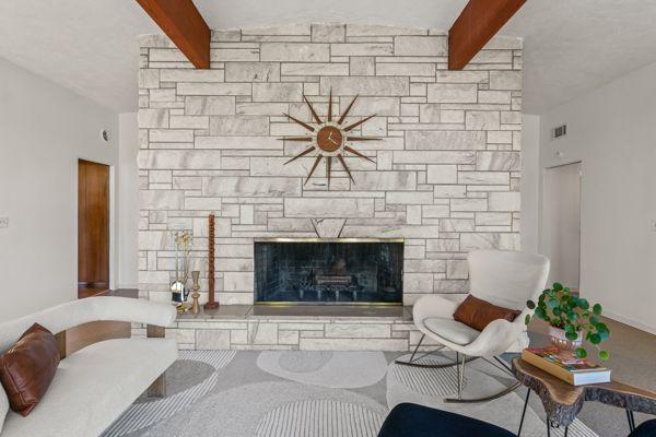 Modern living room with stone fireplace, wood beams, and white furniture
