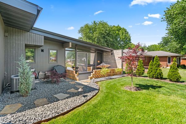 Modern backyard patio with stone landscaping, green lawn, and a covered seating area under blue sky