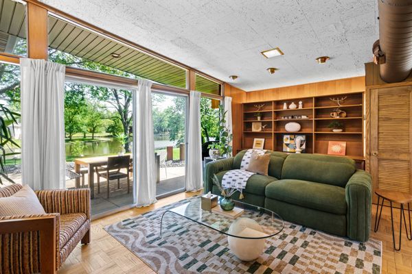 Bright living room with green sofa, wooden shelves, glass table, and large windows overlooking a patio and garden