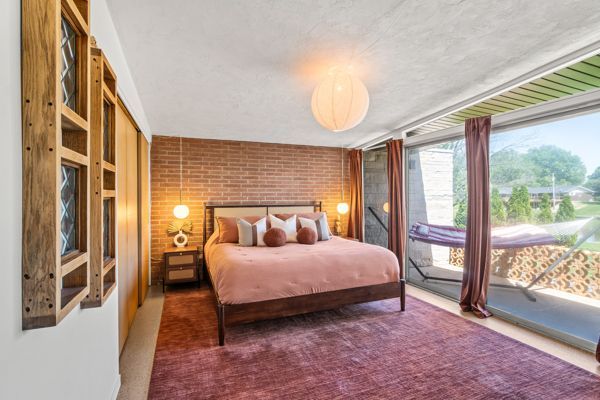 Bright bedroom with a king bed, brick accent wall, and large windows overlooking greenery