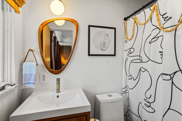 Small bathroom with white sink, gold-framed mirror, toilet, and black line-art shower curtain