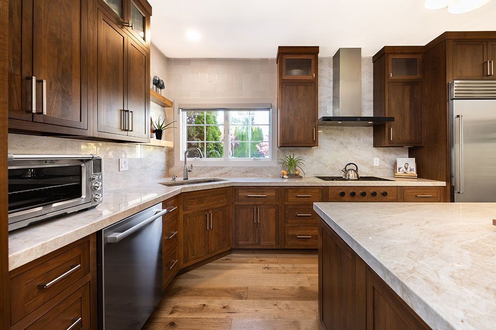 Modern kitchen with dark wood cabinets, light stone countertops, stainless steel appliances, and a window over the sink.