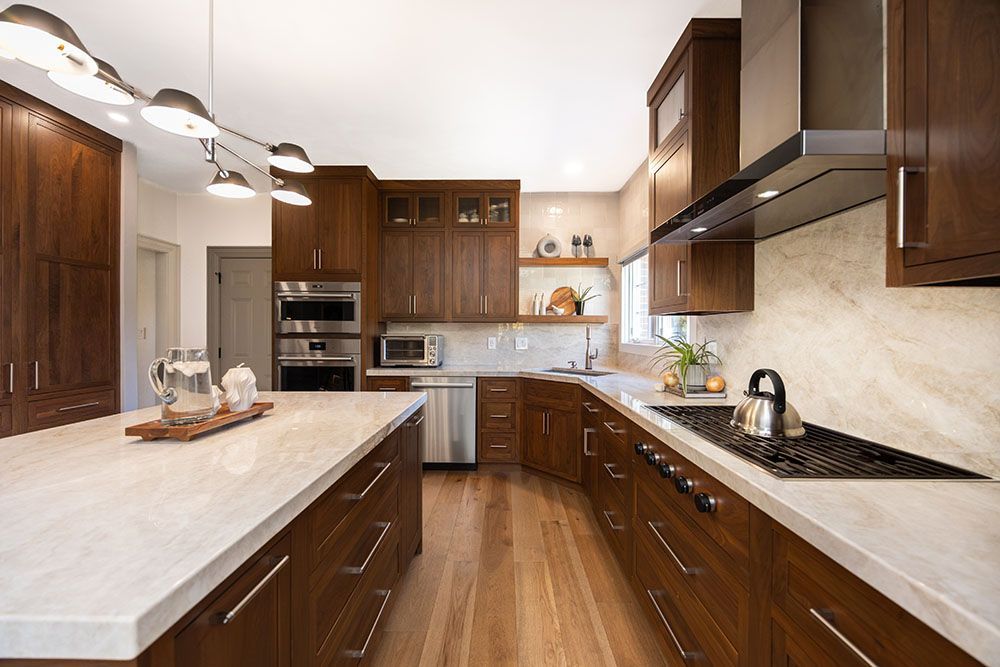 A modern kitchen featuring rich wood cabinets, a large white stone-topped island, and stainless steel appliances.