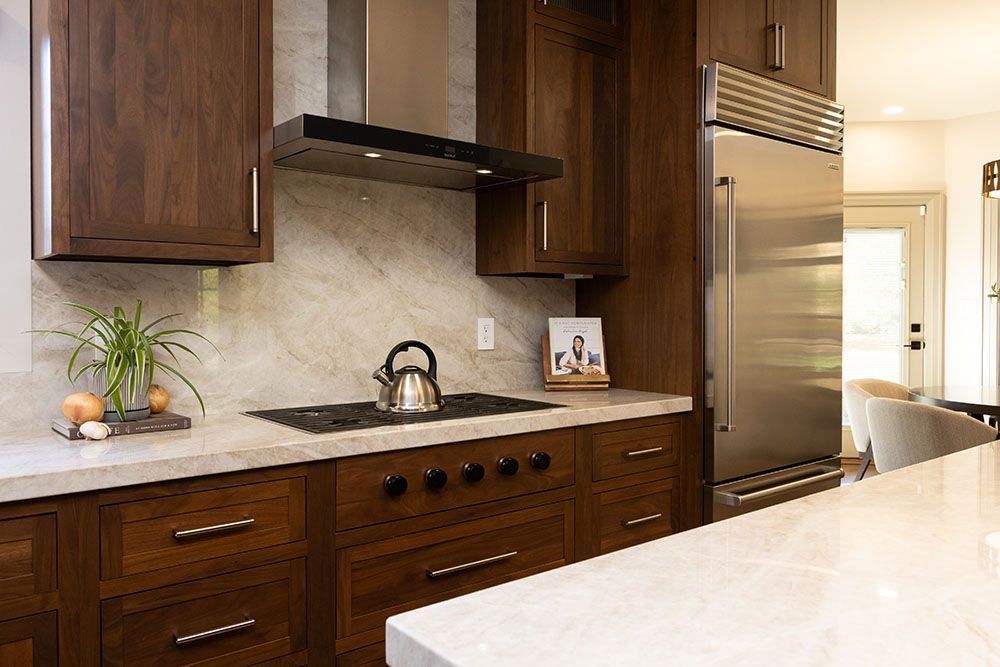 A modern kitchen featuring dark wood cabinets, a marble backsplash, stainless steel appliances, and light countertops.