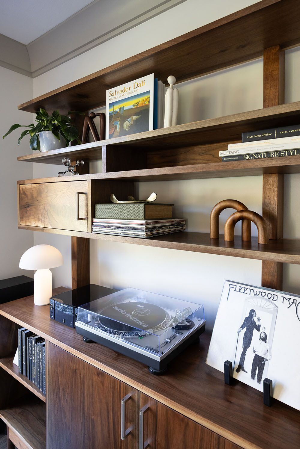 A mid-century modern wooden shelving unit featuring a record player, a vinyl record, decorative objects, and a lamp.