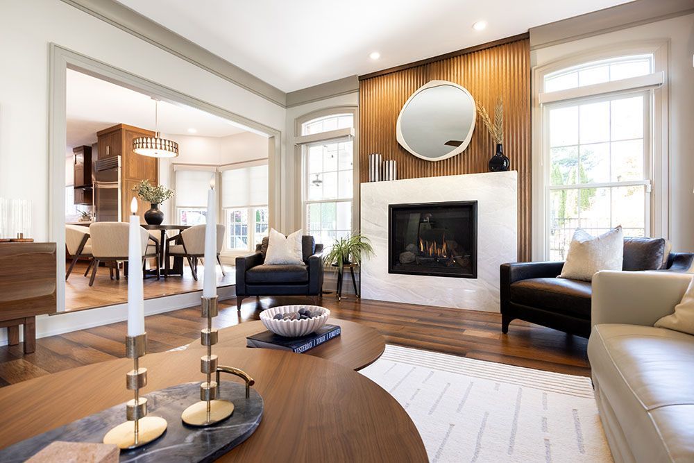 A modern, open-concept living room with a white marble fireplace, wood-slat accent wall, and a wooden coffee table.