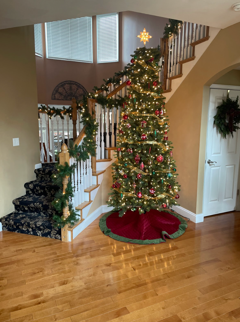 Christmas tree with garland on a staircase in a home. Red tree skirt and holiday decorations.
