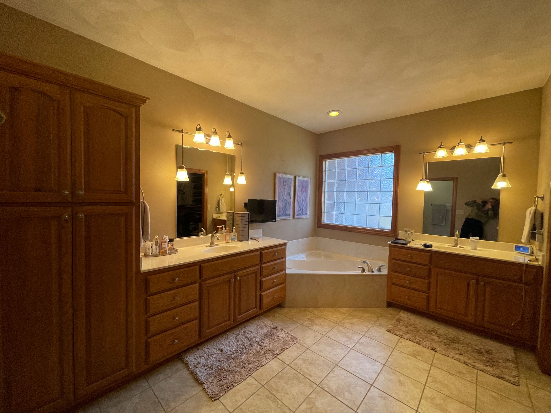 Spacious bathroom with two vanities, a soaking tub, and wooden cabinets. Beige walls and tile flooring.