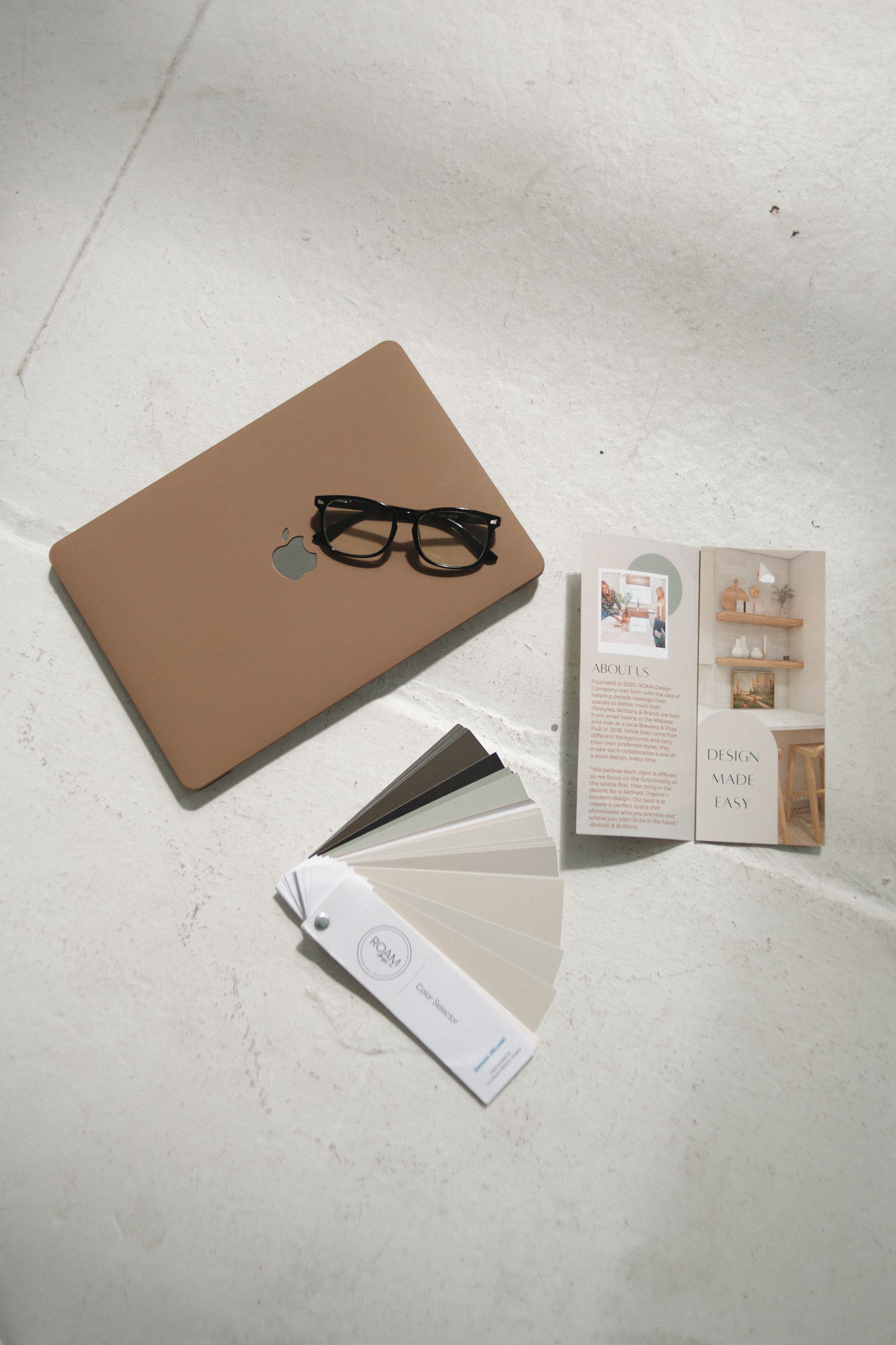 Laptop, glasses, paint swatches, and small toy set on a white surface.