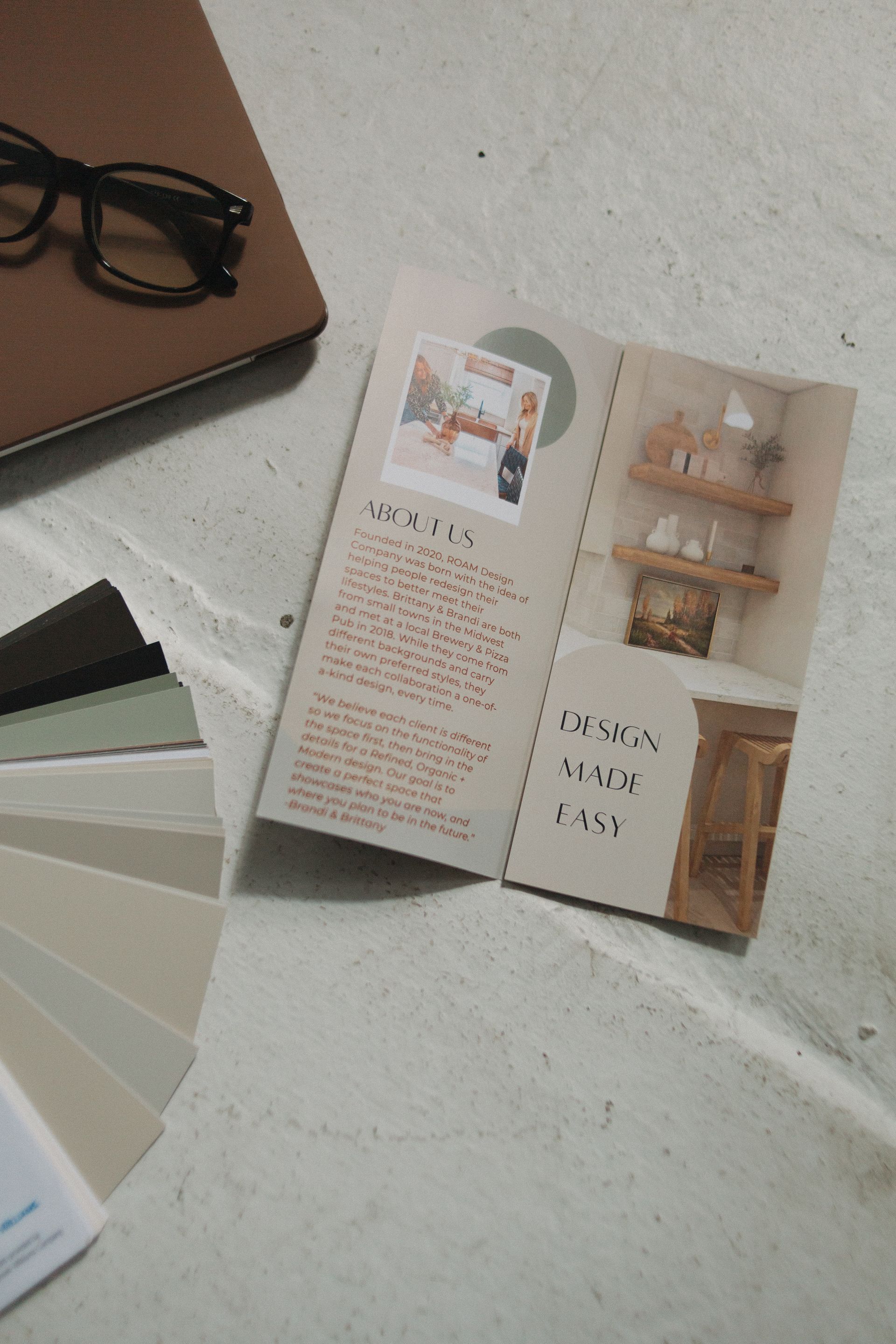 Brochure, paint swatches, eyeglasses, and notebook on a stone surface.