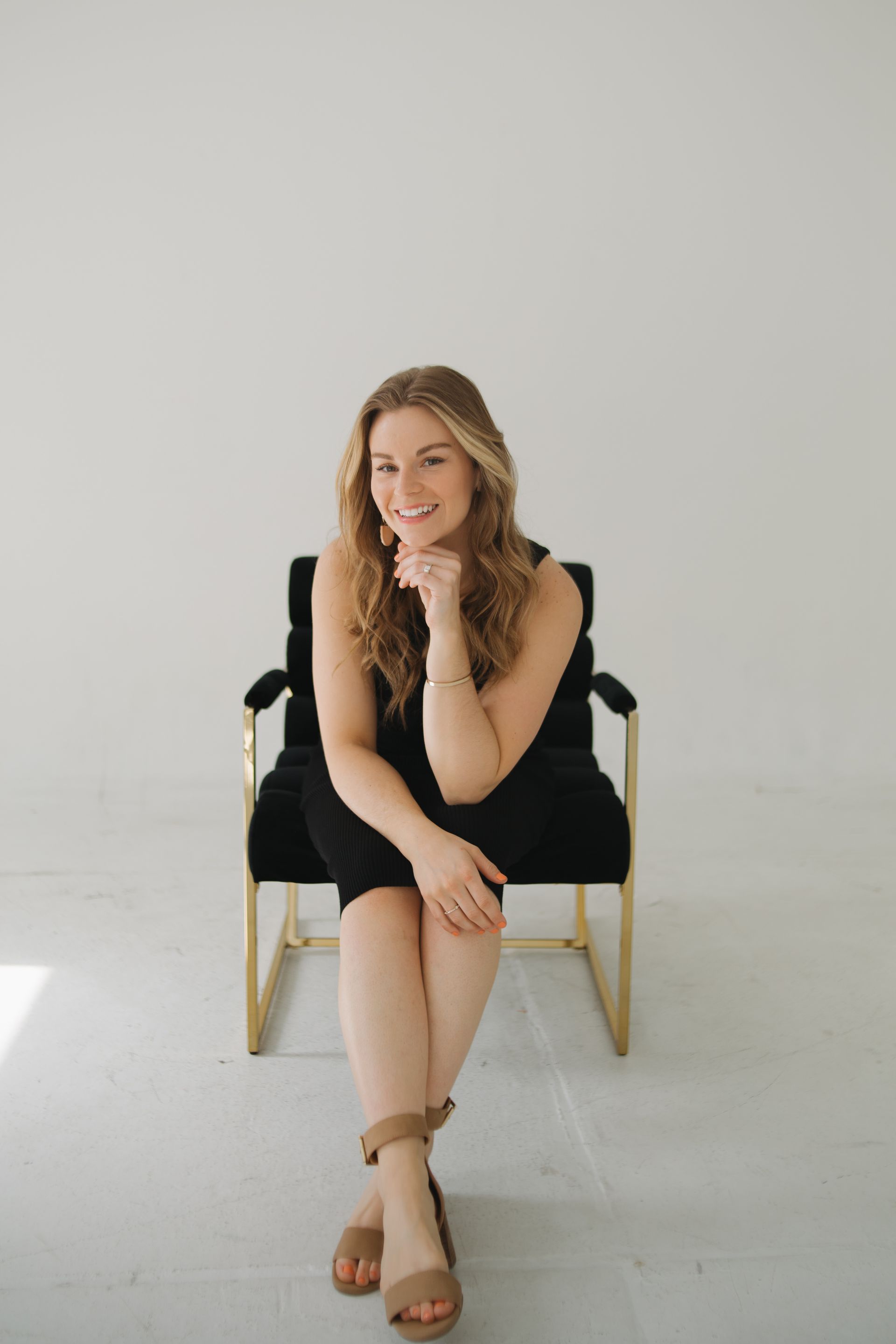 Woman in black dress sitting in modern chair, smiling, indoors.