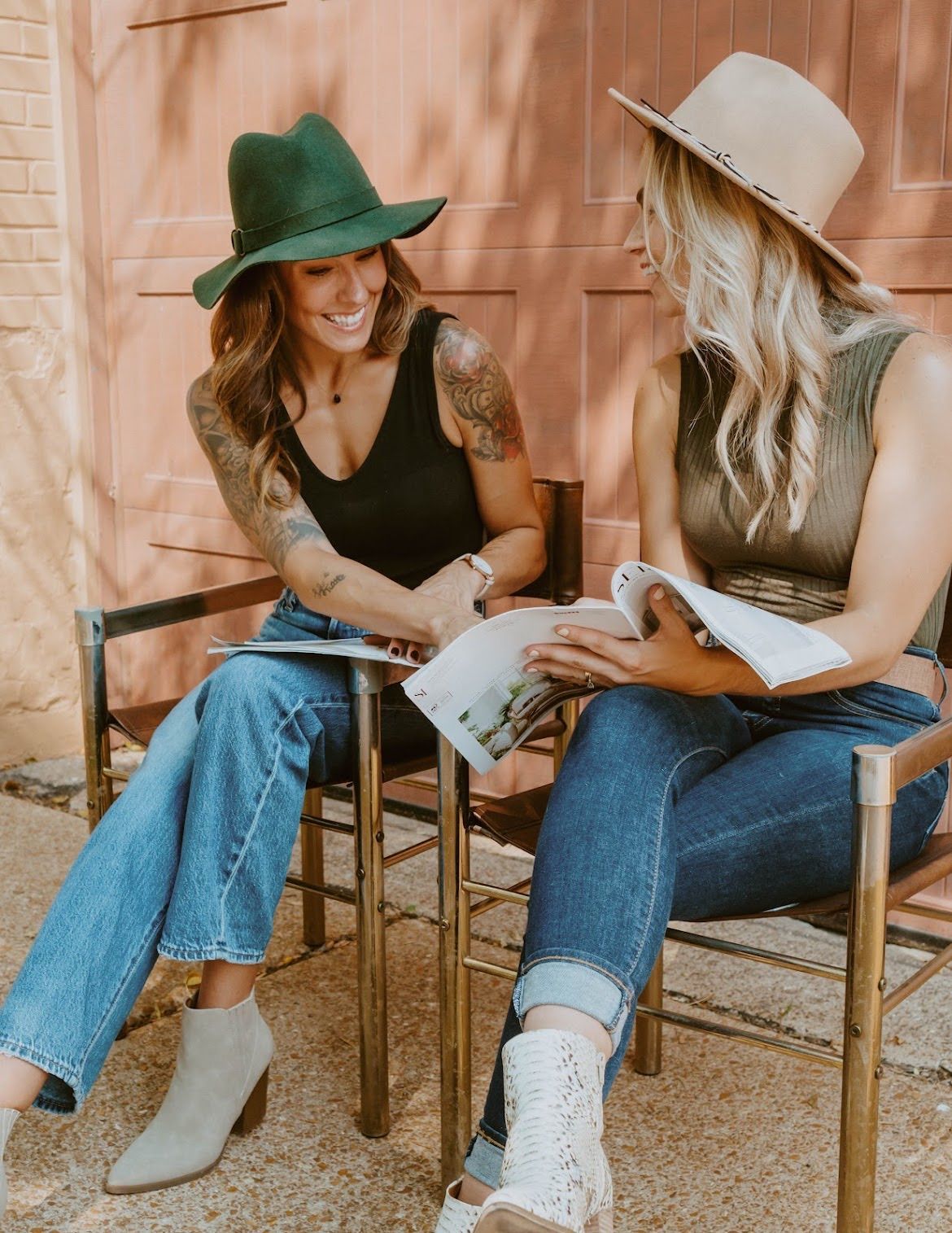 Two women in hats seated, reading outdoors. One in green, one in tan. Sunny.