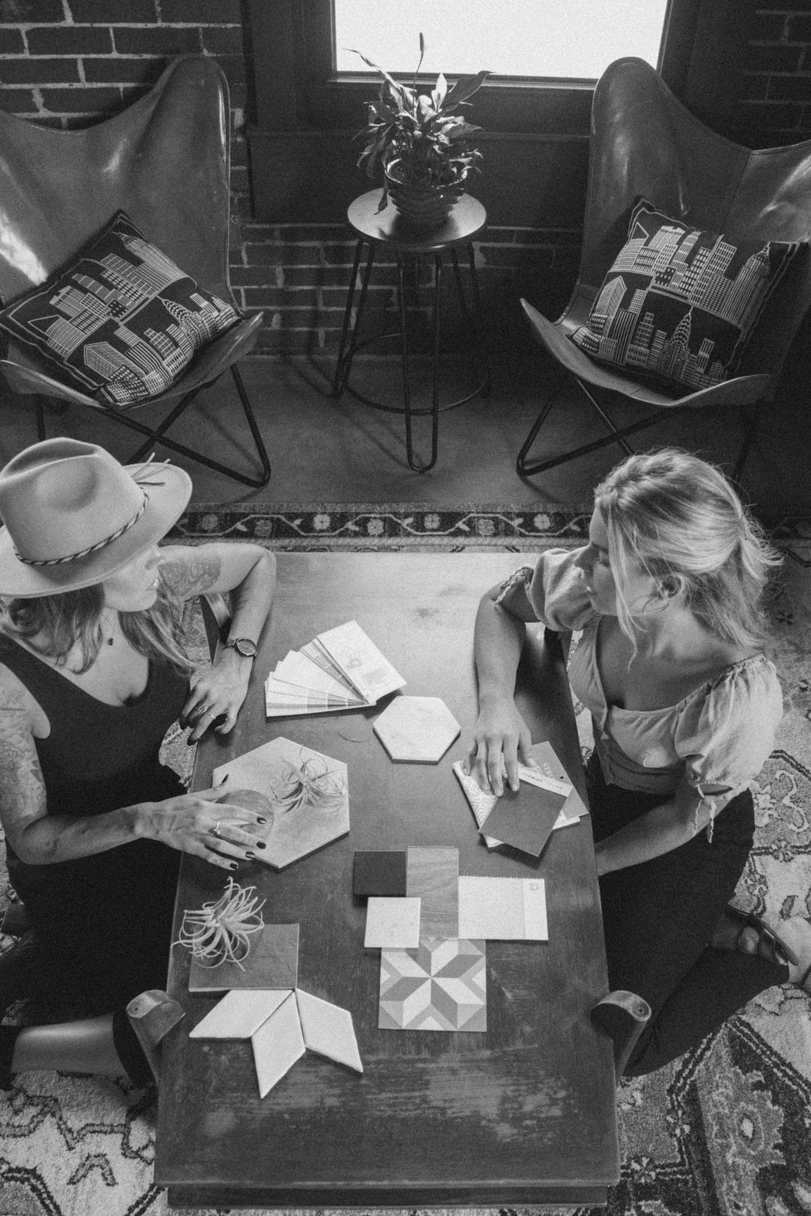 Two women at table with tile samples, leather chairs, and floral arrangement.