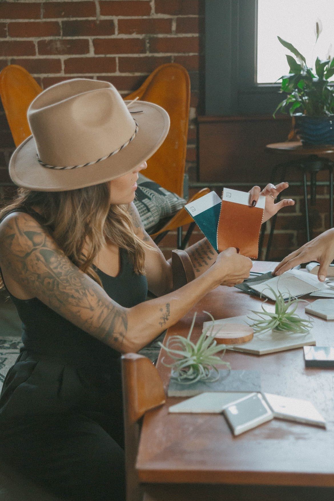 Woman in hat reviews fabric samples at table.