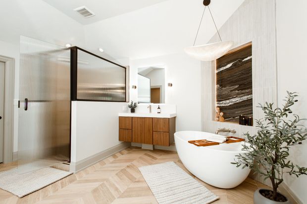 Modern bathroom with a glass shower, wooden vanity, freestanding tub, and herringbone floor.