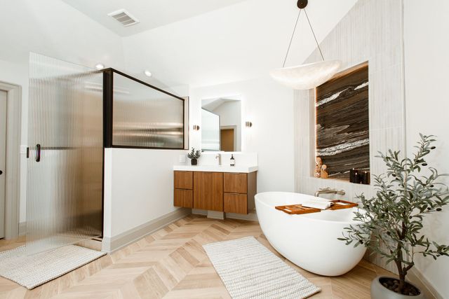 Modern bathroom with a glass shower, wooden vanity, freestanding tub, and herringbone floor.