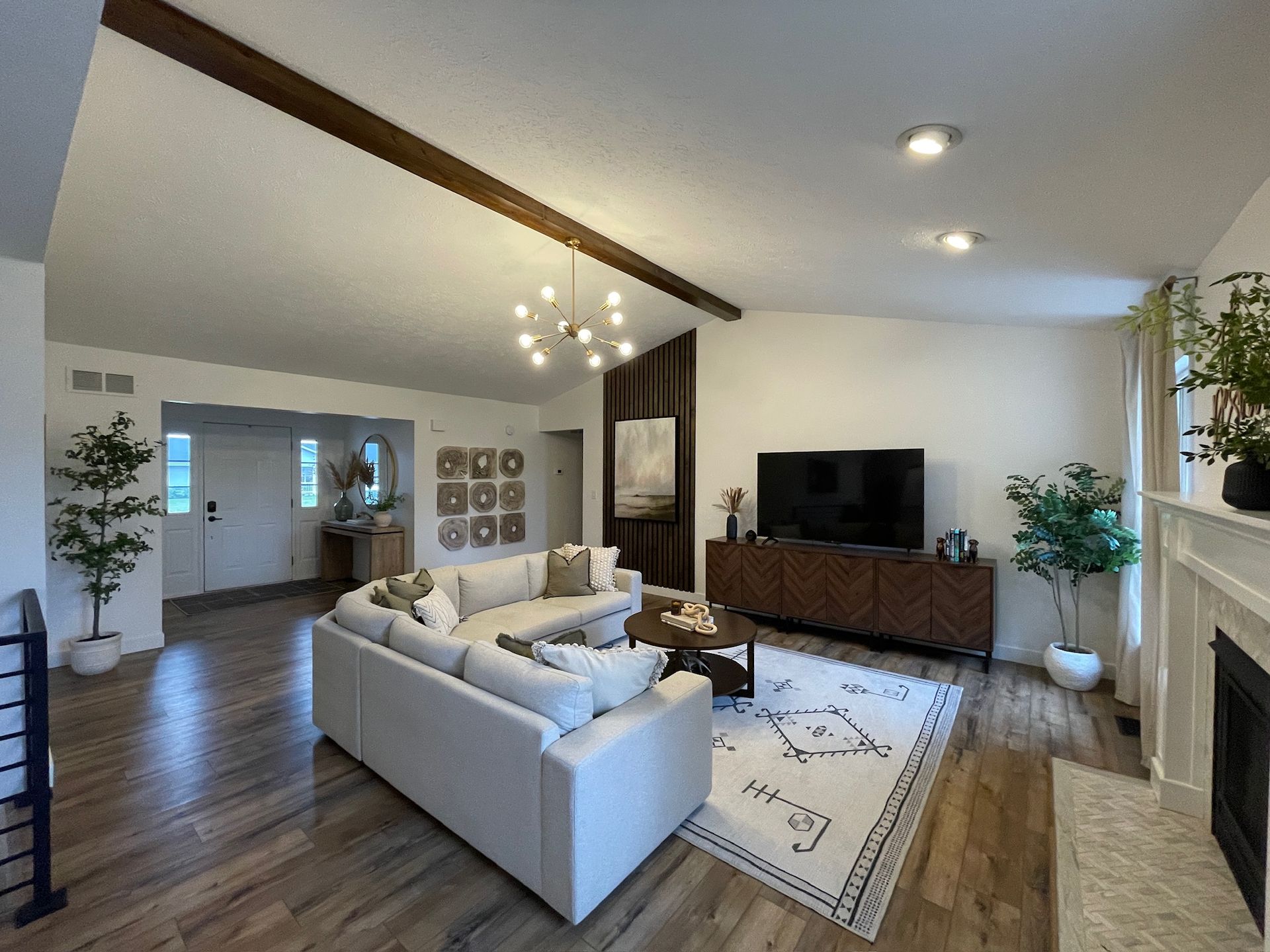Spacious living room with white walls, wood floors, sectional sofa, fireplace, and TV cabinet.