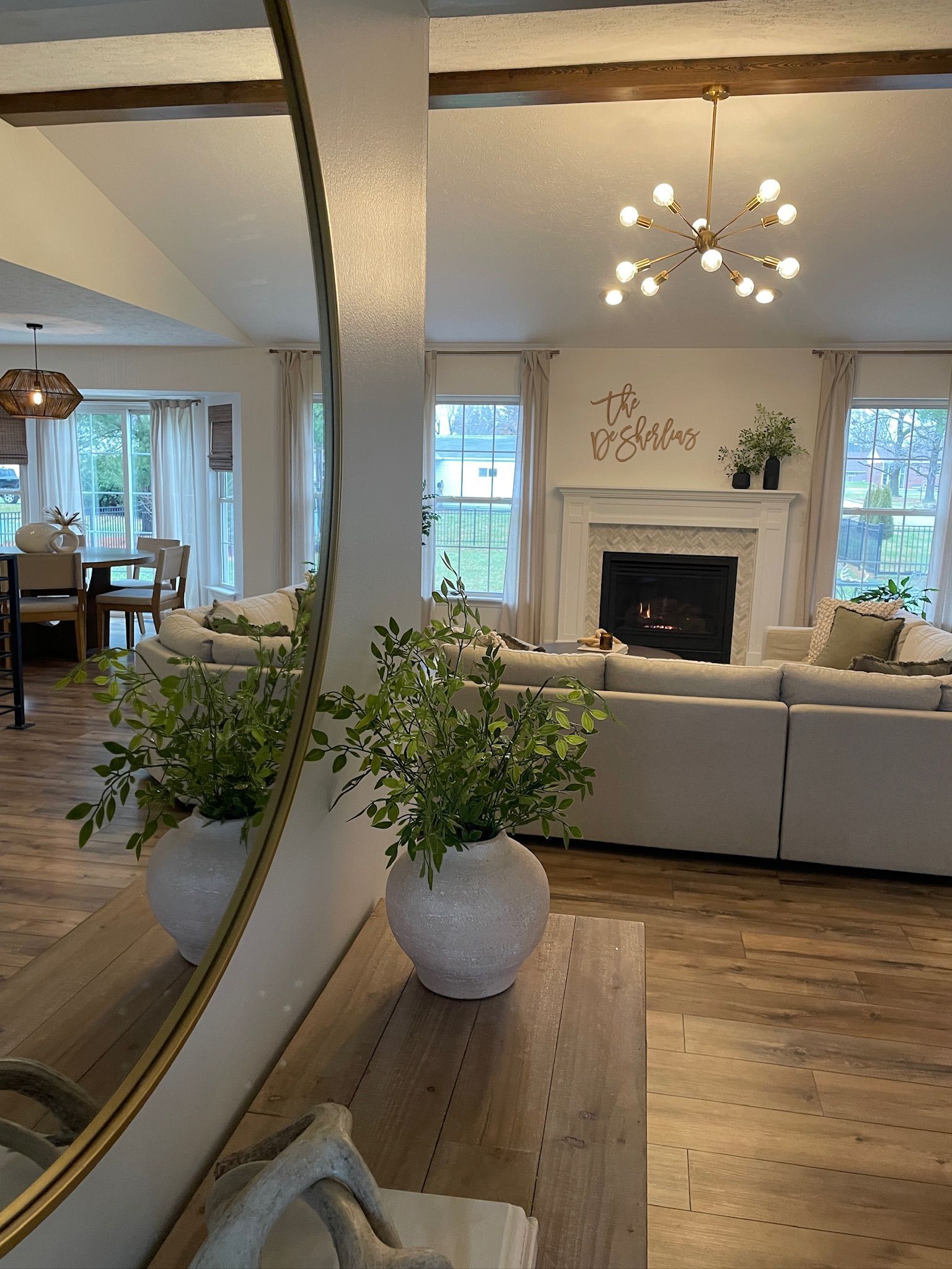Interior with living room and dining area, neutral tones, large mirror, fireplace, and green plants.