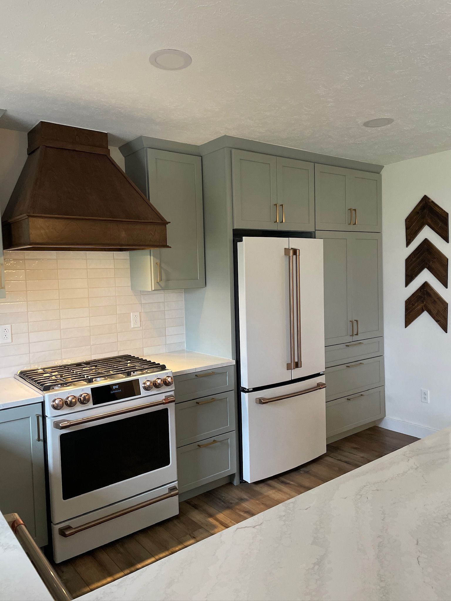 A modern kitchen with sage green cabinets, copper range hood, and white appliances.