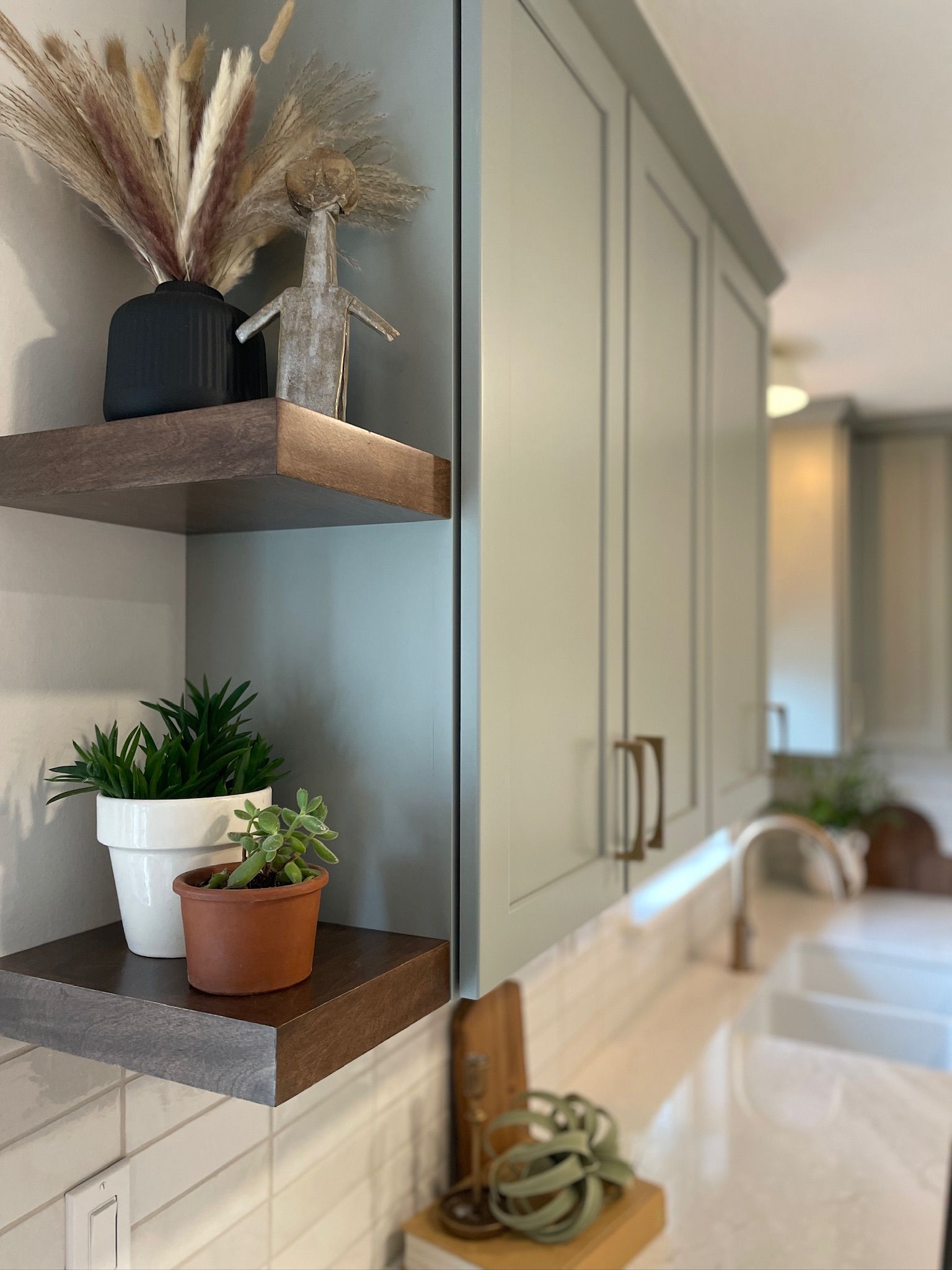 Kitchen corner with open shelving and light blue cabinets. Shelves hold plants and vases; countertop with a sink.