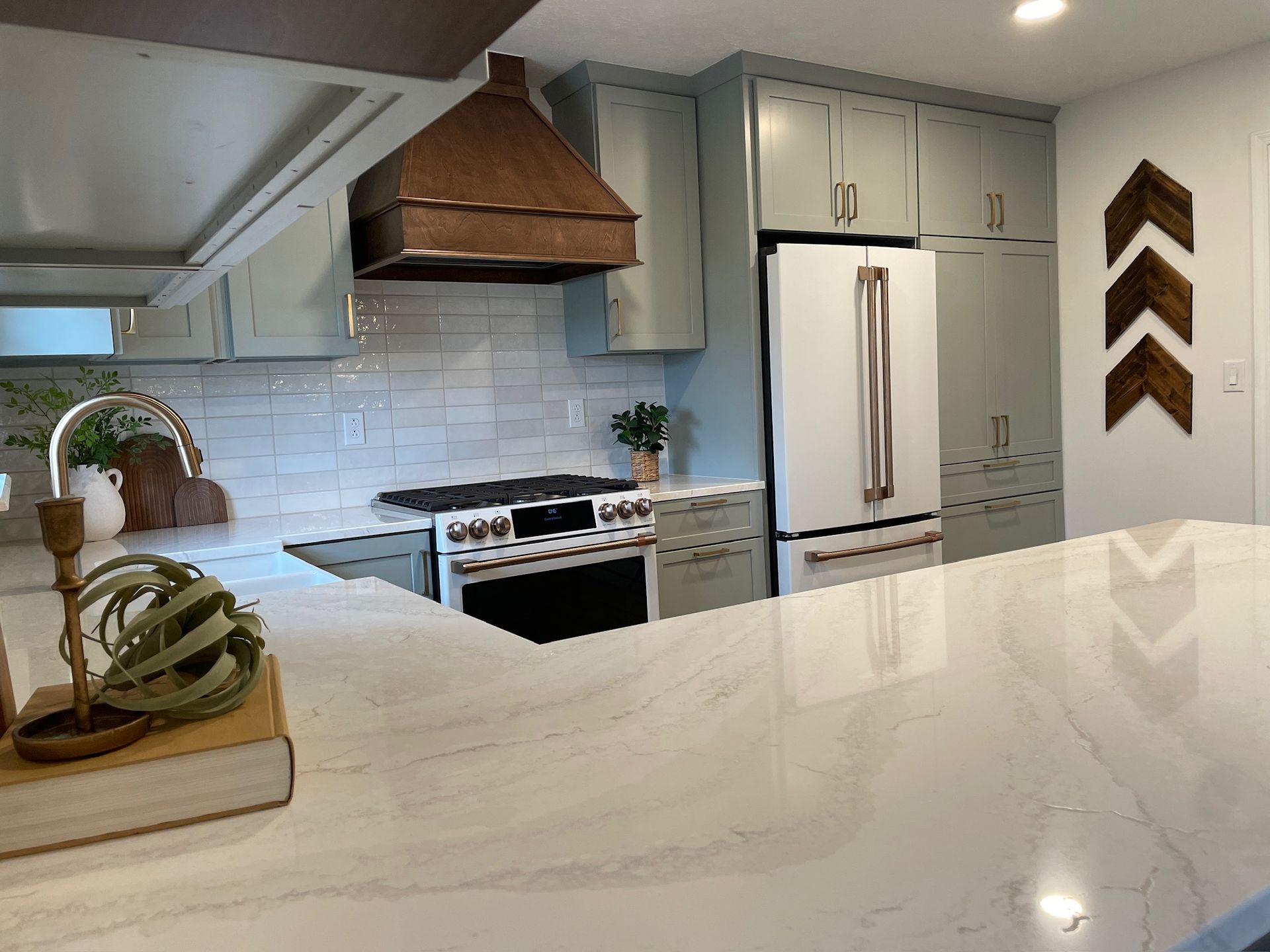 Kitchen with light blue cabinets, copper hood, white countertops, and decorative wooden arrows on the wall.