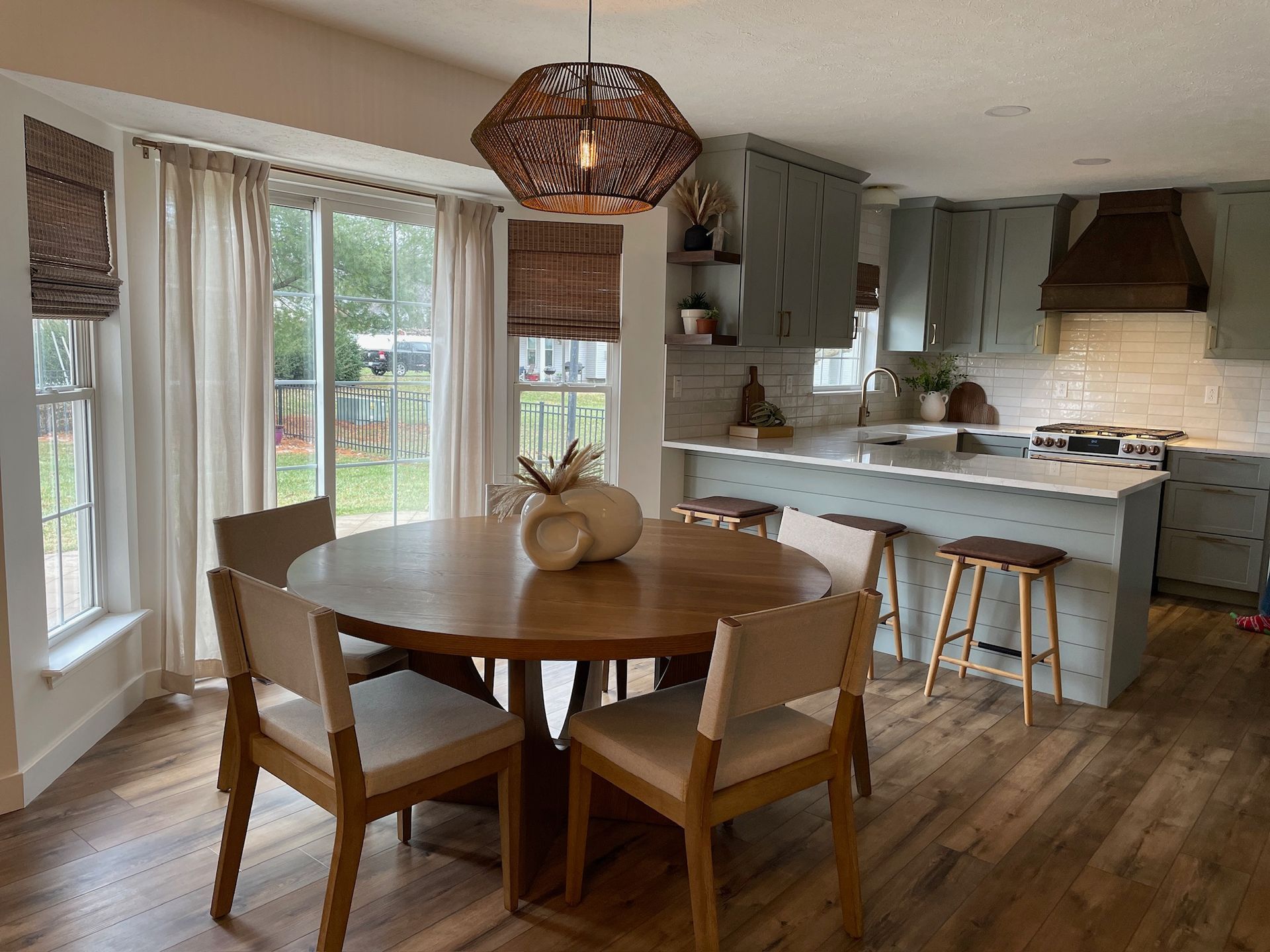 Kitchen with wooden floor, round table with chairs, and blue cabinets. Sliding glass door and woven light fixture.