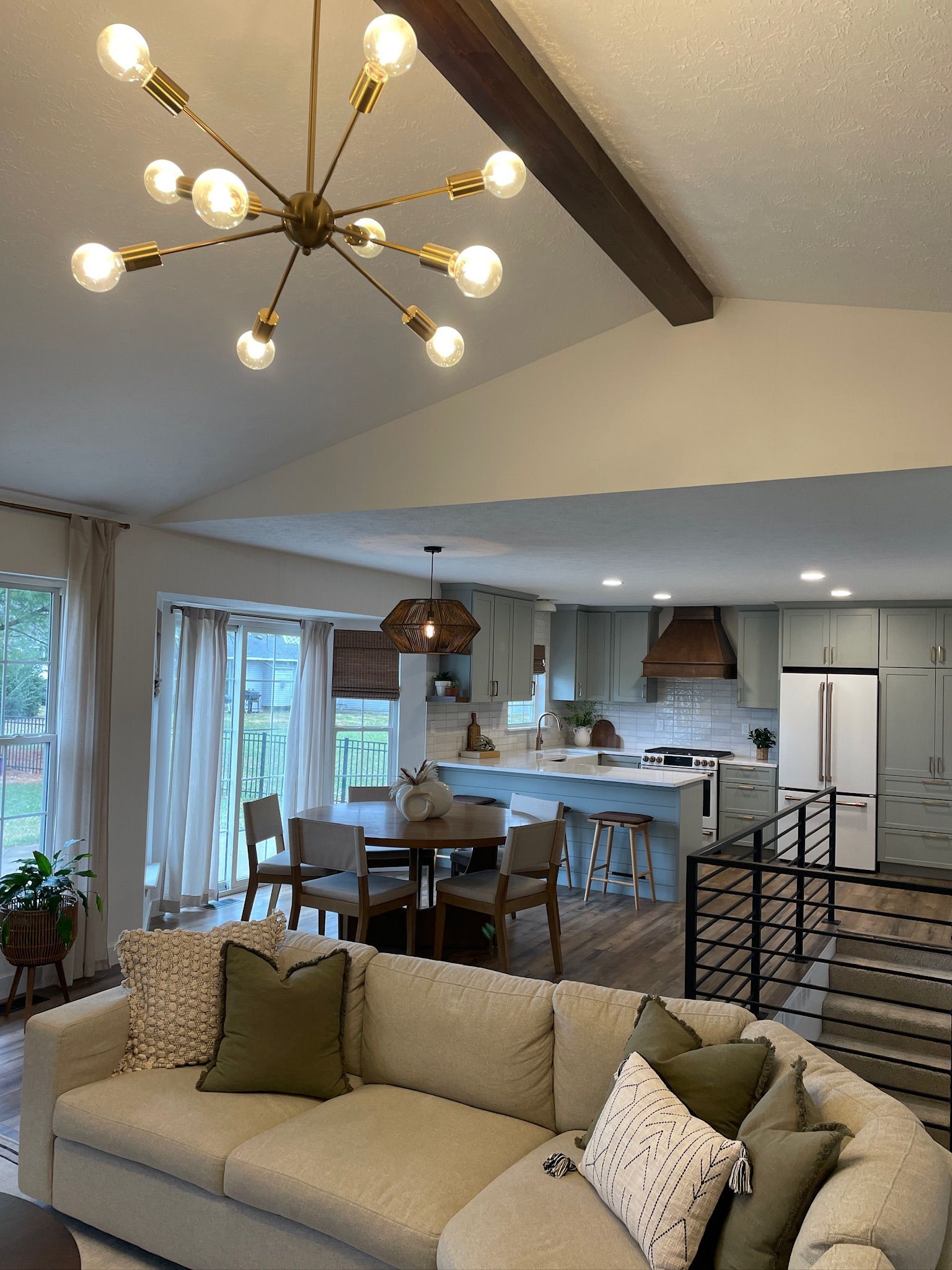 Living room with a sectional sofa, a Sputnik chandelier, and an open kitchen with blue cabinets.