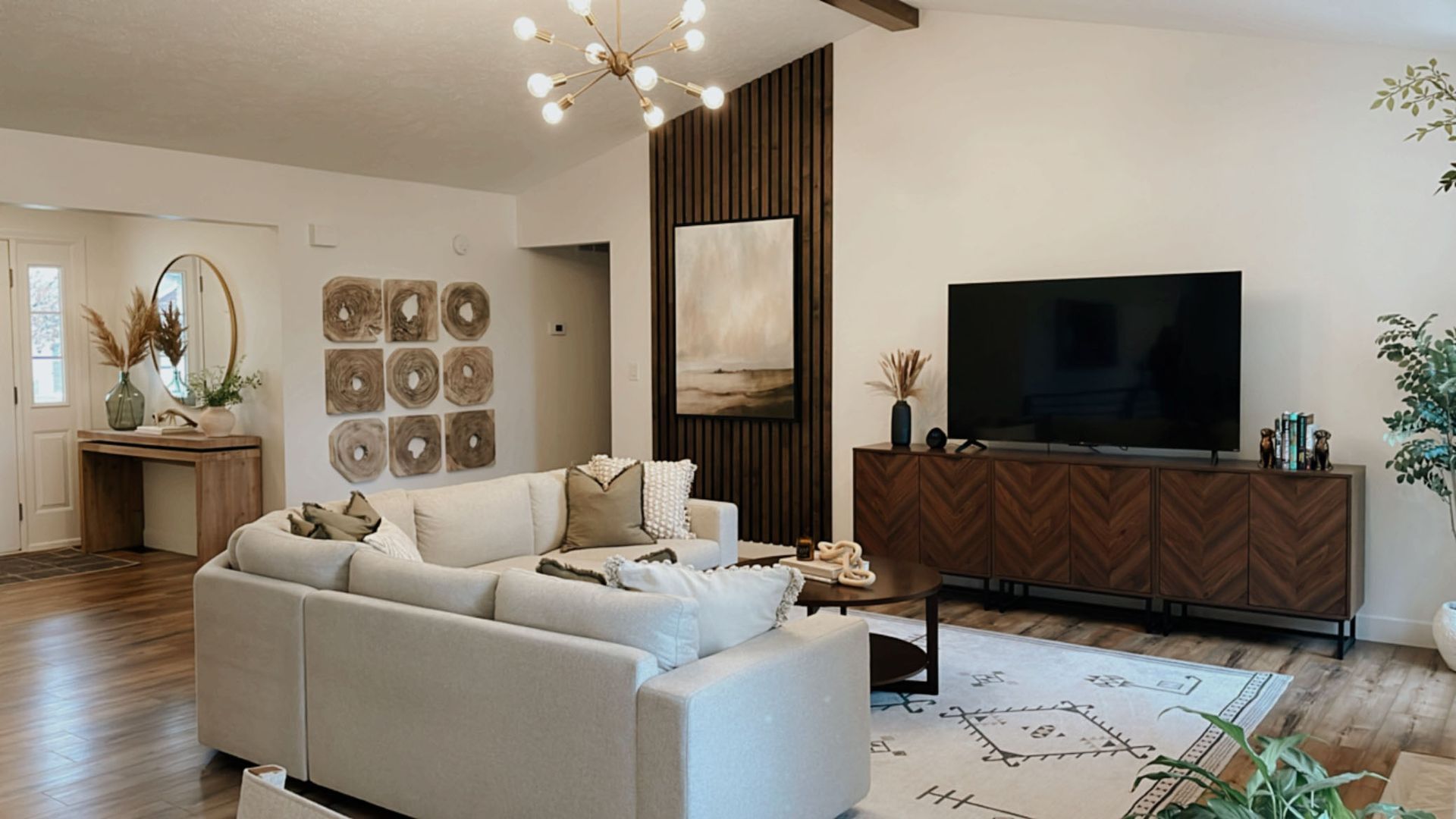 Living room with white sectional, wood accents, and large TV.