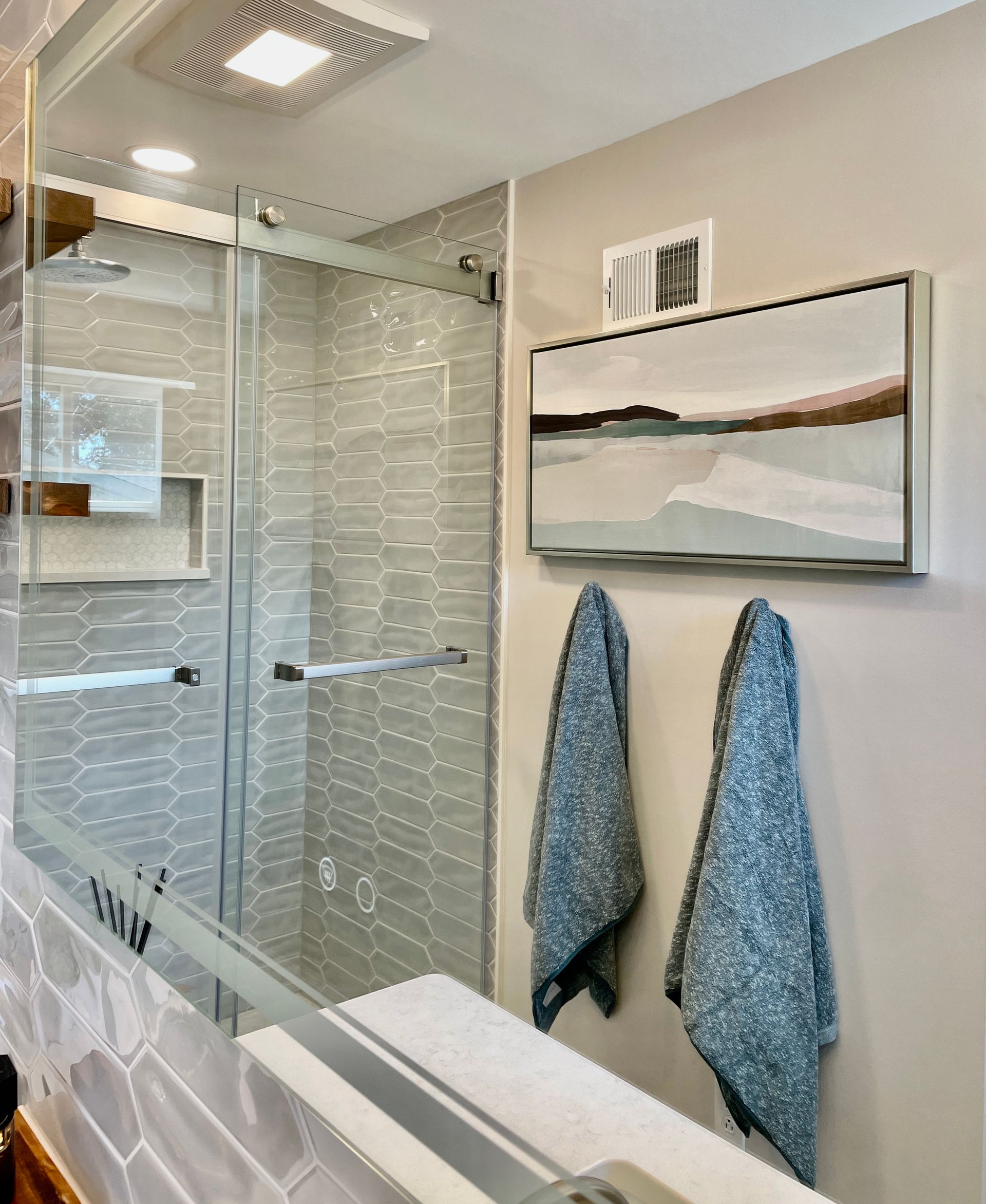 Modern bathroom with a glass shower, art, and two blue towels. Gray and beige tones.