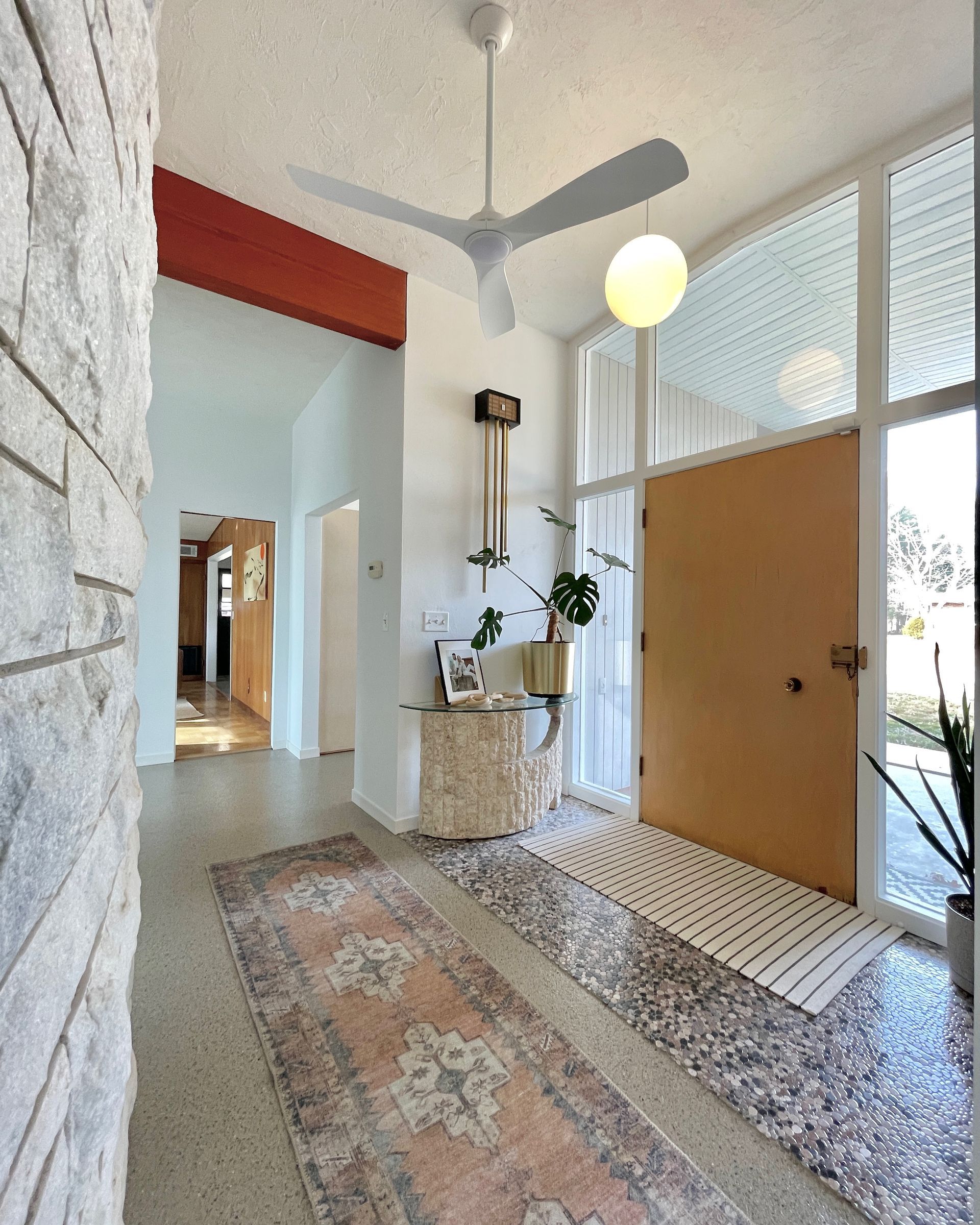 Entryway with white walls, stone wall, tan door, rug, and ceiling fan.