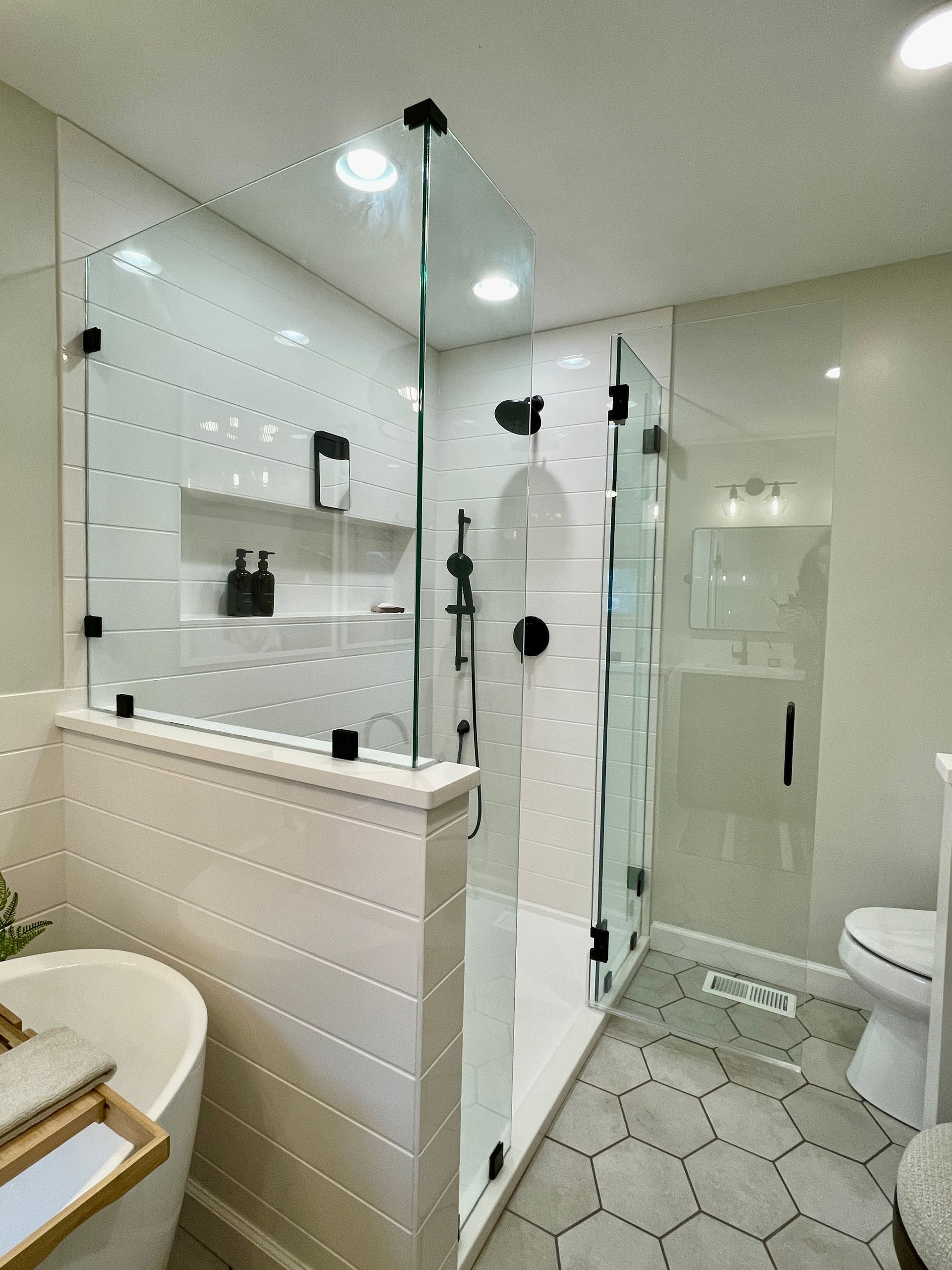 Modern bathroom with a glass shower, white tile, and hexagon floor.
