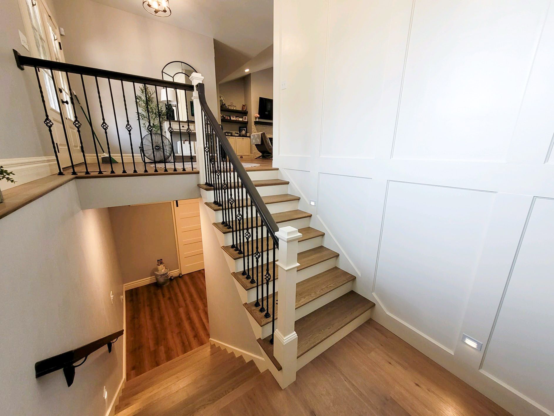 Hallway with hardwood floor, shoe storage, chandelier, custom wall moulding molding, white walls, traditional design, remodel and removation in Caseyville o'fallon il, and staircase with black railing, leading to a lower level.