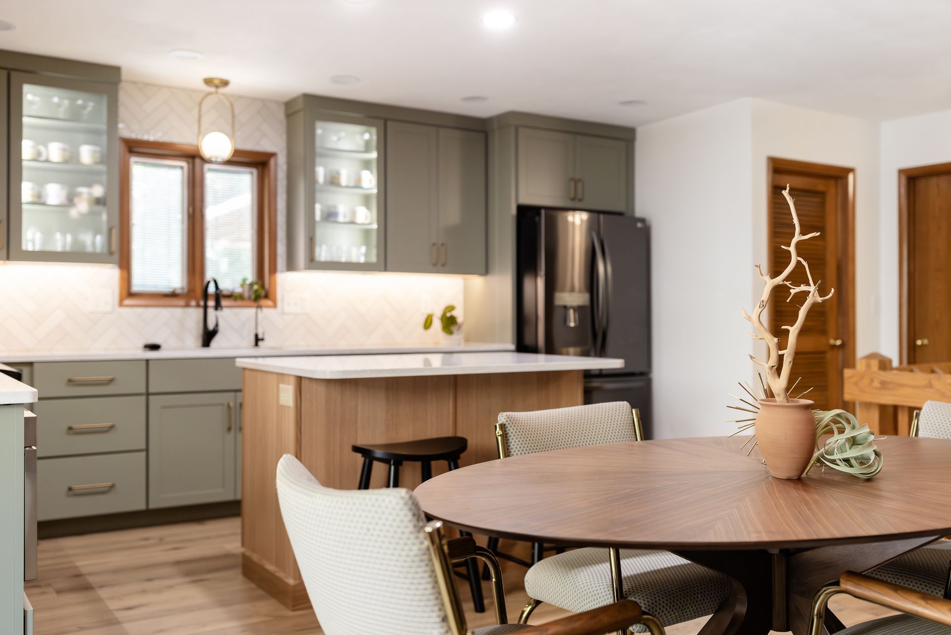 Kitchen with green cabinets, wood island, round table, and black refrigerator.