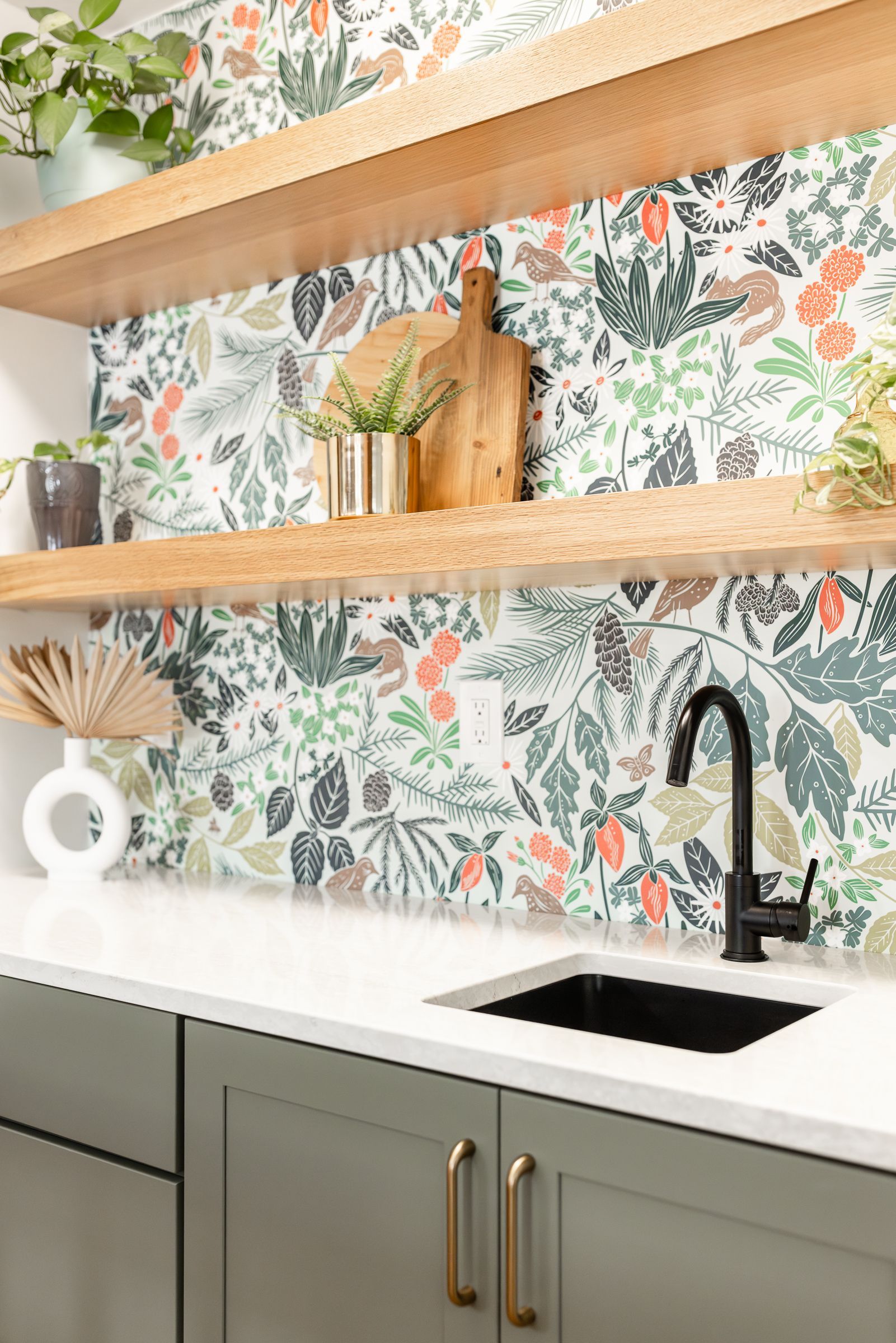 Kitchen with floral wallpaper backsplash, wooden shelves, and gray cabinets.