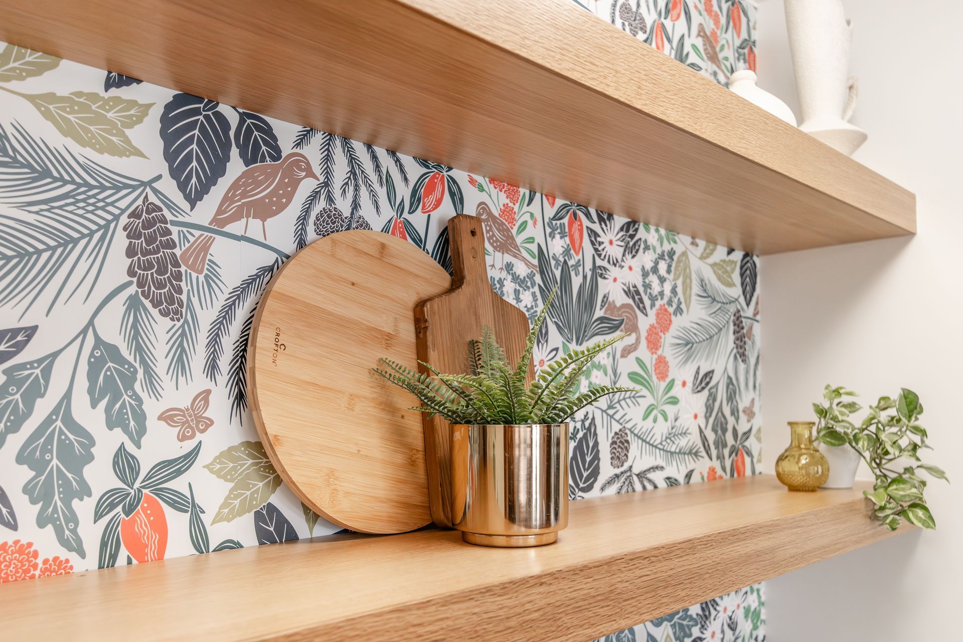 Wooden shelves with decor against a botanical print wallpaper.
