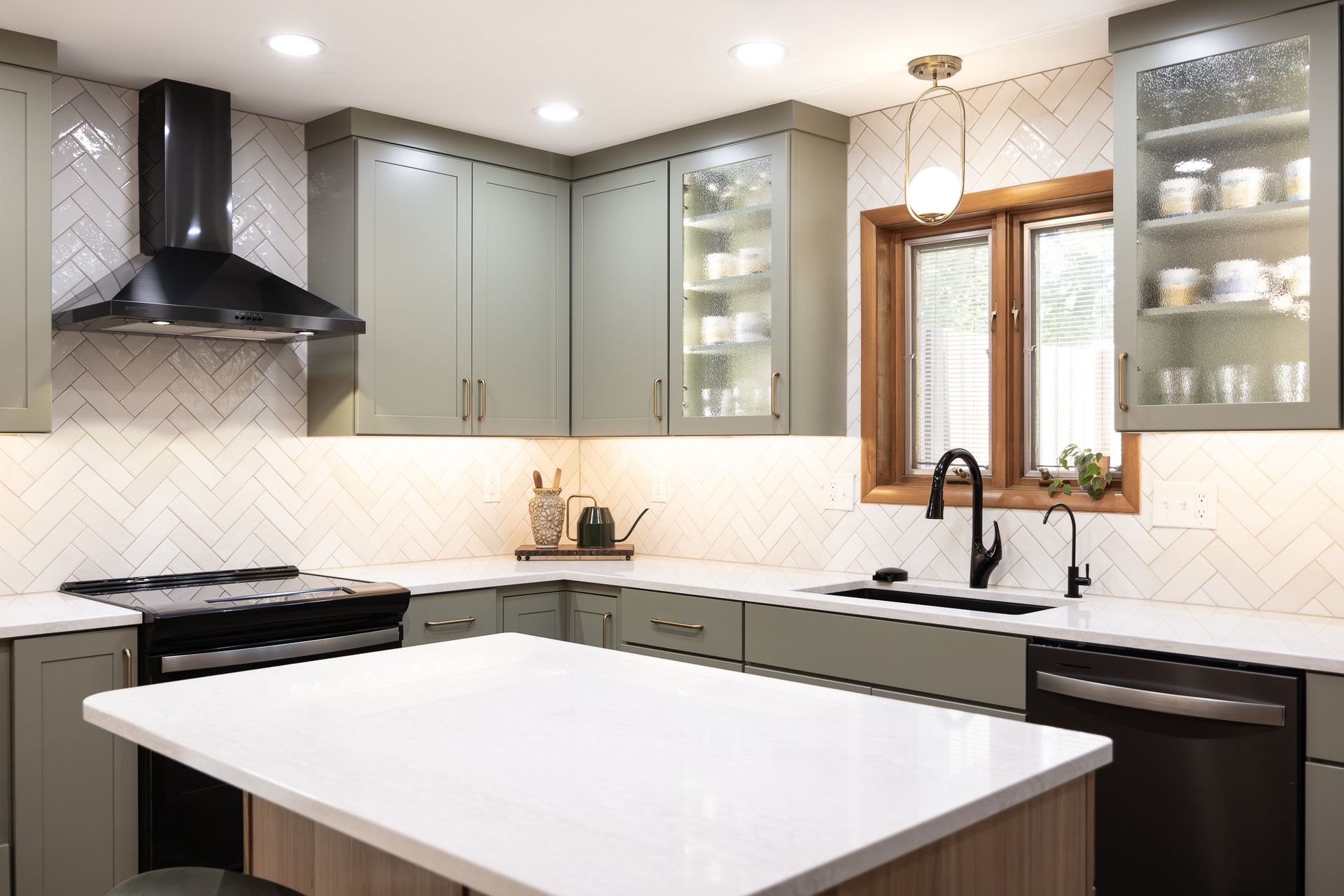 Modern kitchen with sage green cabinets, white countertops, and herringbone backsplash.