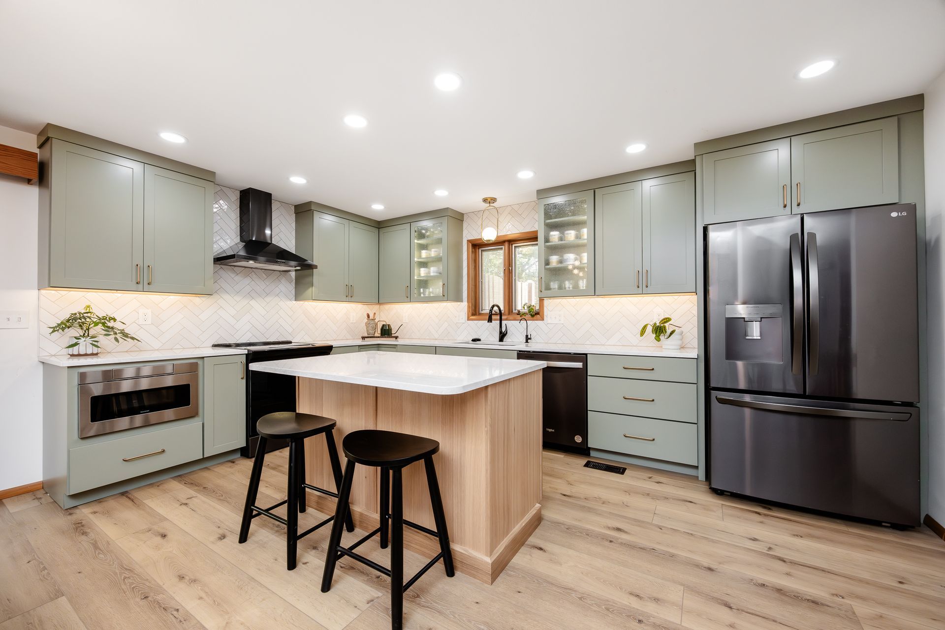 Modern kitchen with sage green cabinets, light wood island, stainless steel appliances, and wood flooring.