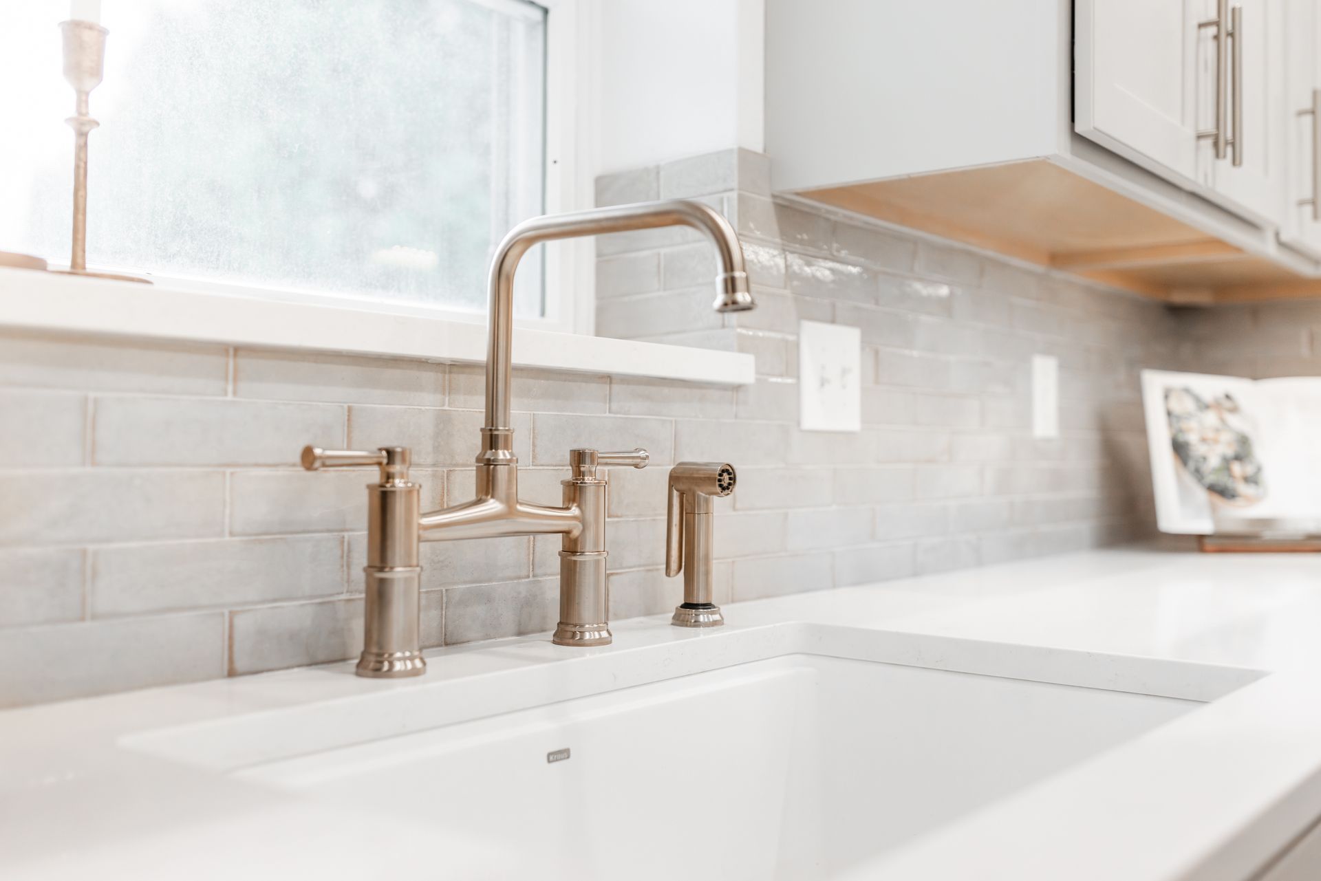 Kitchen faucet over a white sink, with a gray tile backsplash and cabinets in the background.