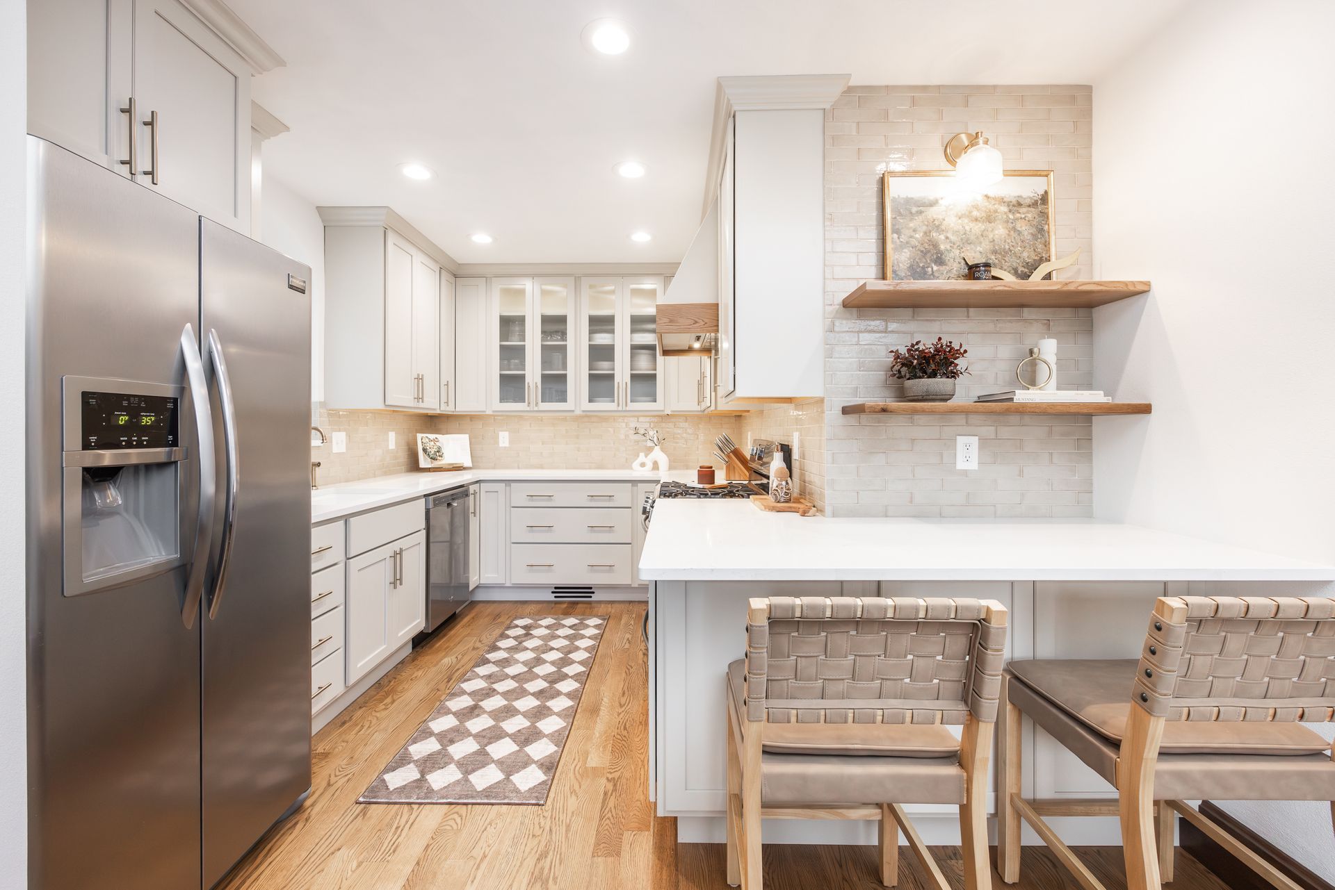 Modern kitchen with light grey cabinets, stainless steel fridge, and breakfast bar with woven stools.